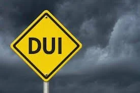 Yellow warning sign with black text reading 'DUI' against a dark, cloudy sky.