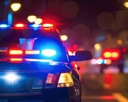 A police car with flashing red and blue lights at night, on a road with blurred lights in the background.