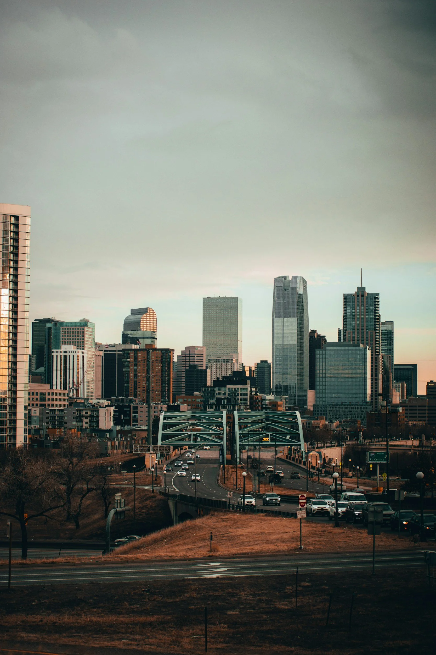 City skyline with tall skyscrapers and a busy road in the foreground during sunset.