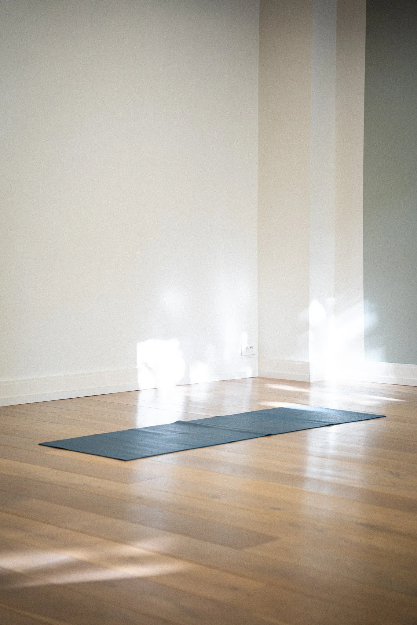 Tapis de yoga noir dans une pièce lumineuse avec un sol en bois et un mur blanc.