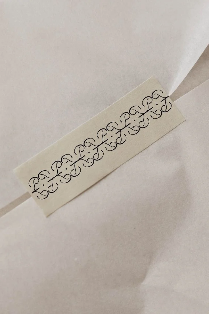 Une étiquette blanche avec un motif noir complexe, collée en diagonale sur une surface blanche.