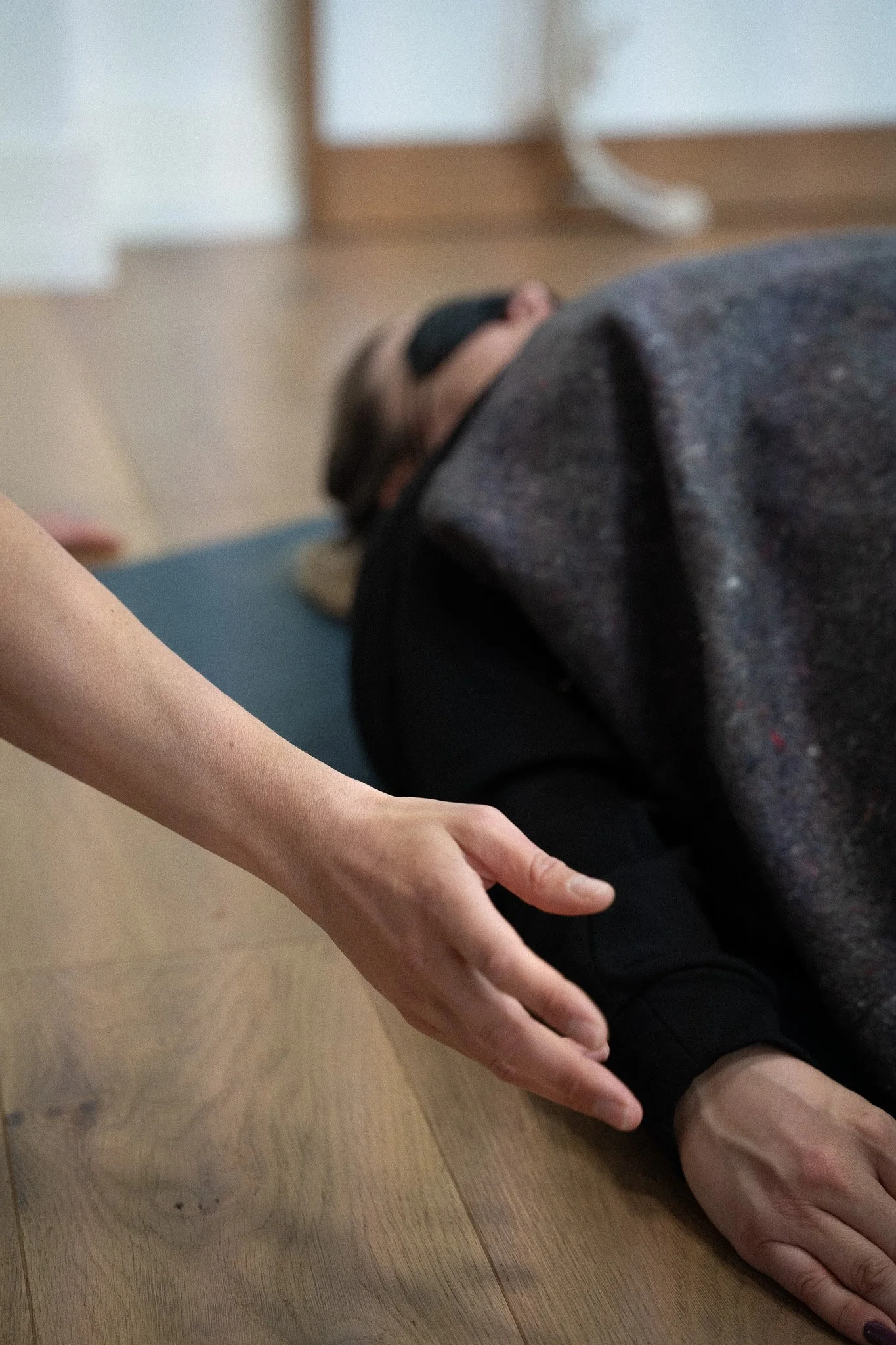 Une personne effectue un mouvement énergétique d'accompagnement à une personne en séance de breathwork en groupe, allongée et portant un masque de sommeil, dans un environnement intérieur.