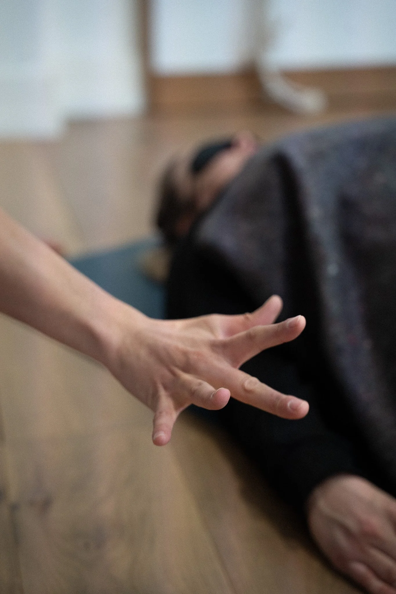Une personne allongée sur le sol avec un masque, en pleine session de breathwork, une autre personne tendant la main en direction de l'autre.