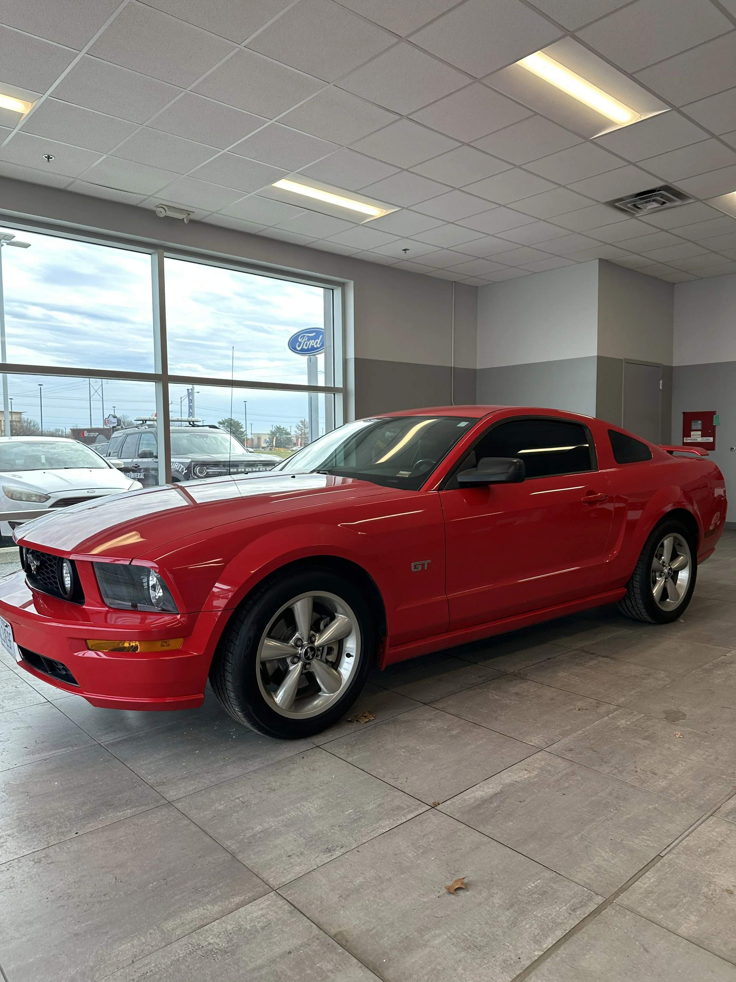 A Tinted Red Ford Mustang GT inside a car dealership showroom.