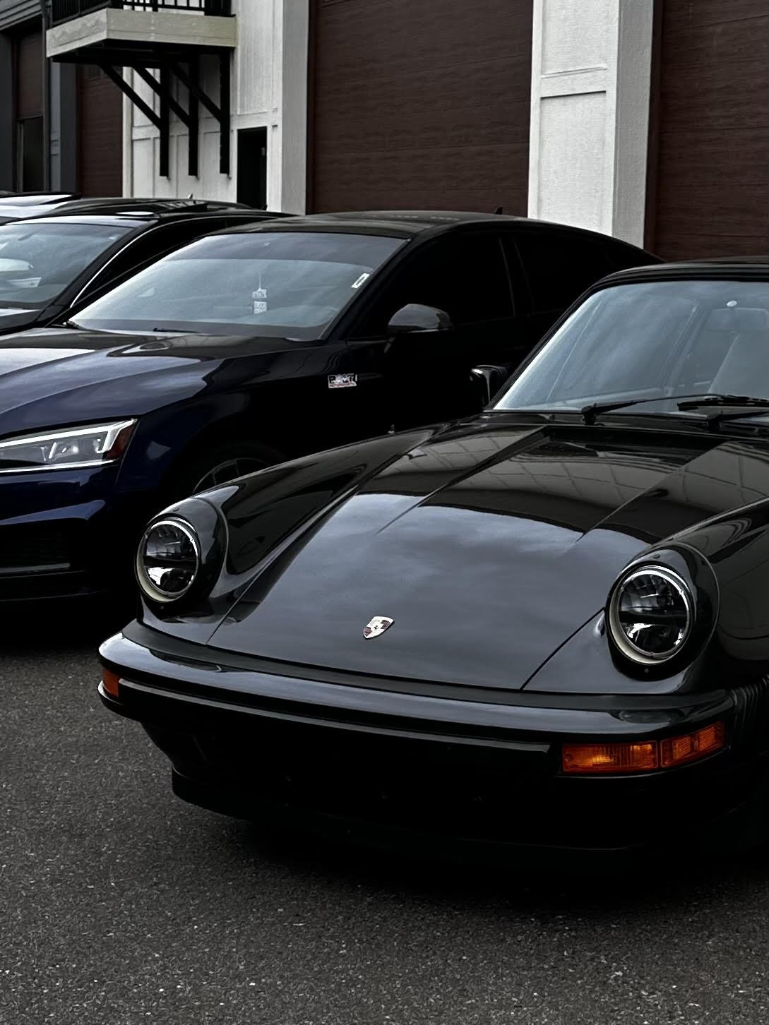 Black Porsche sports car parked among other vehicles outside a building.