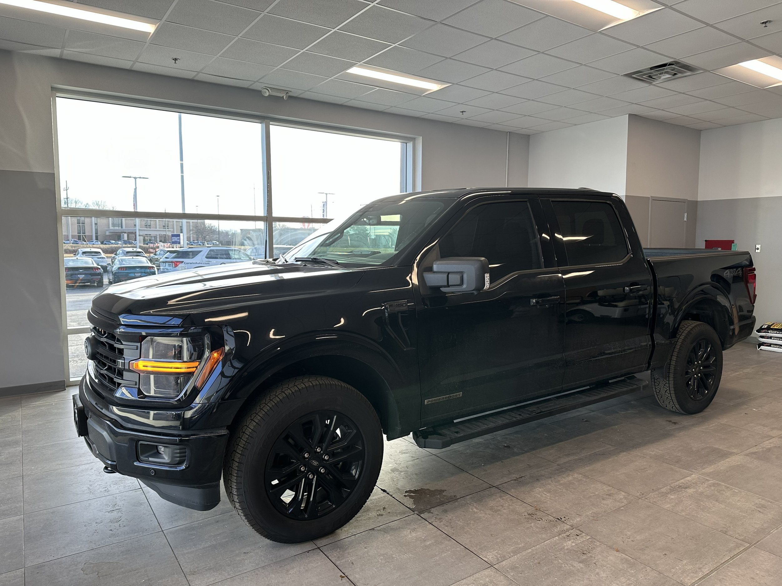 A black pickup truck inside a car dealership showroom with tinted windows.