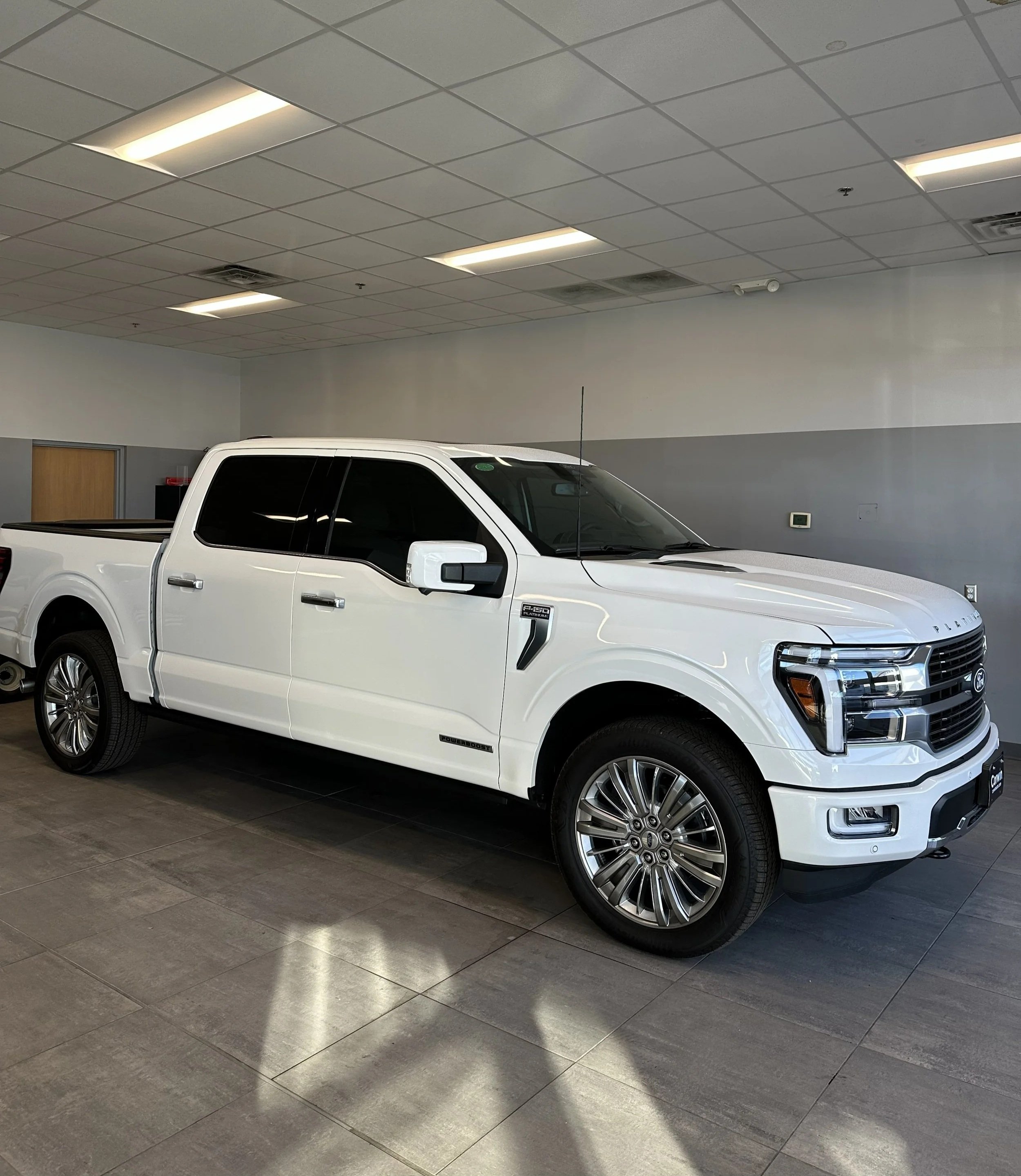 A white Ford F-150 pickup truck inside a showroom With tinted windows.