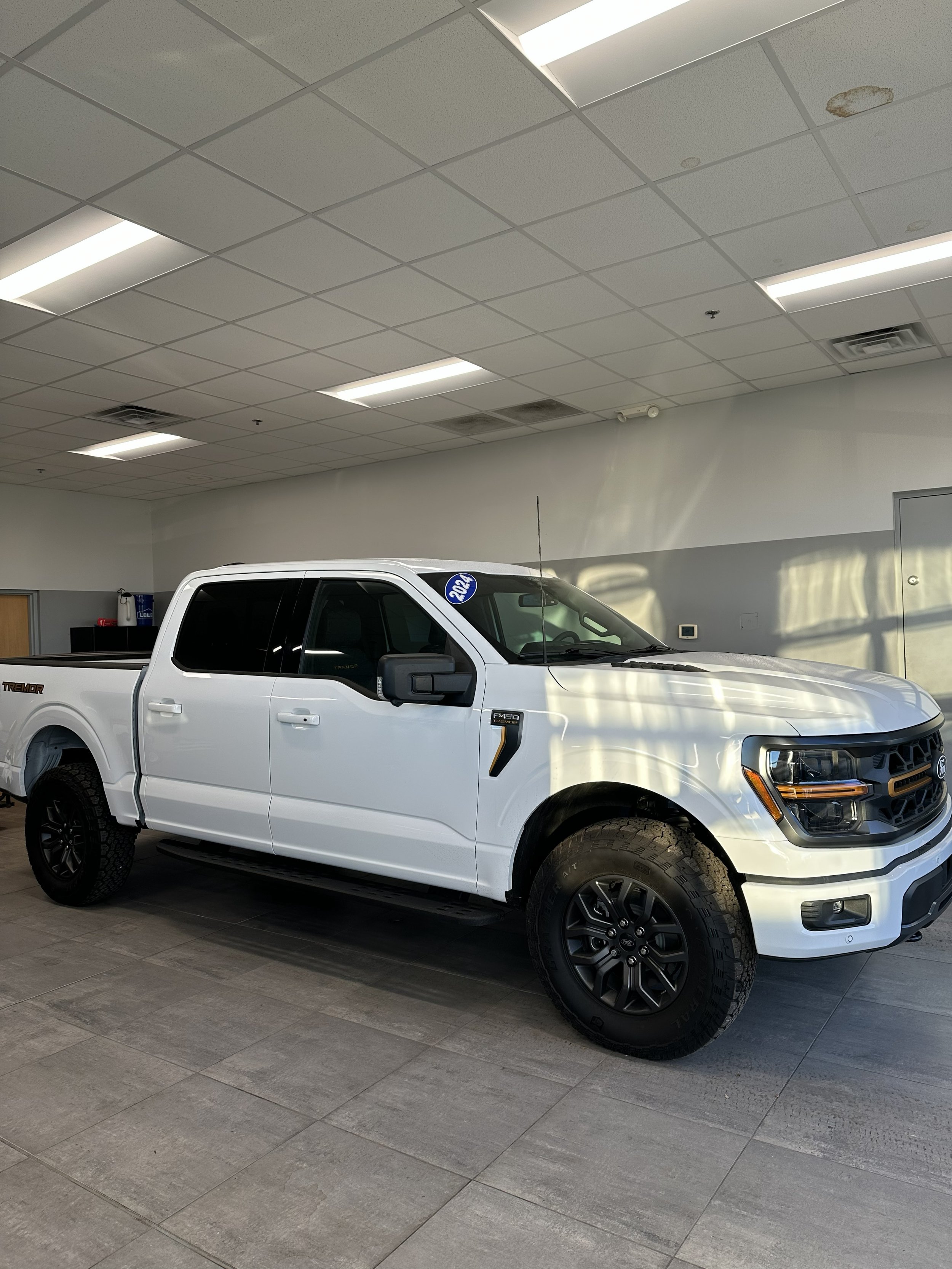 A white 2022 Ford F-150 pickup truck inside a showroom with Tinted Windows.