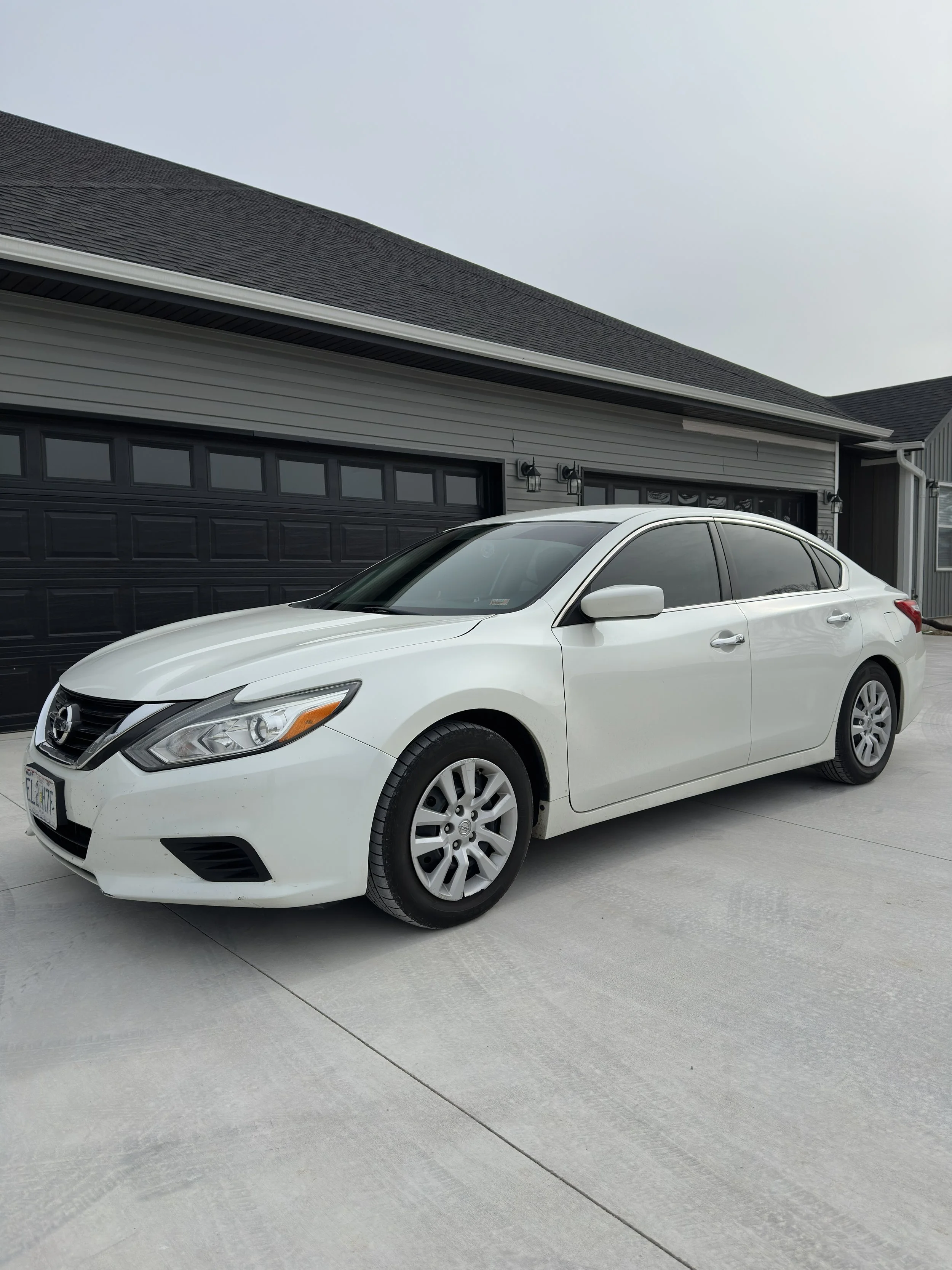 White sedan car parked in front of a house with tinted windows.