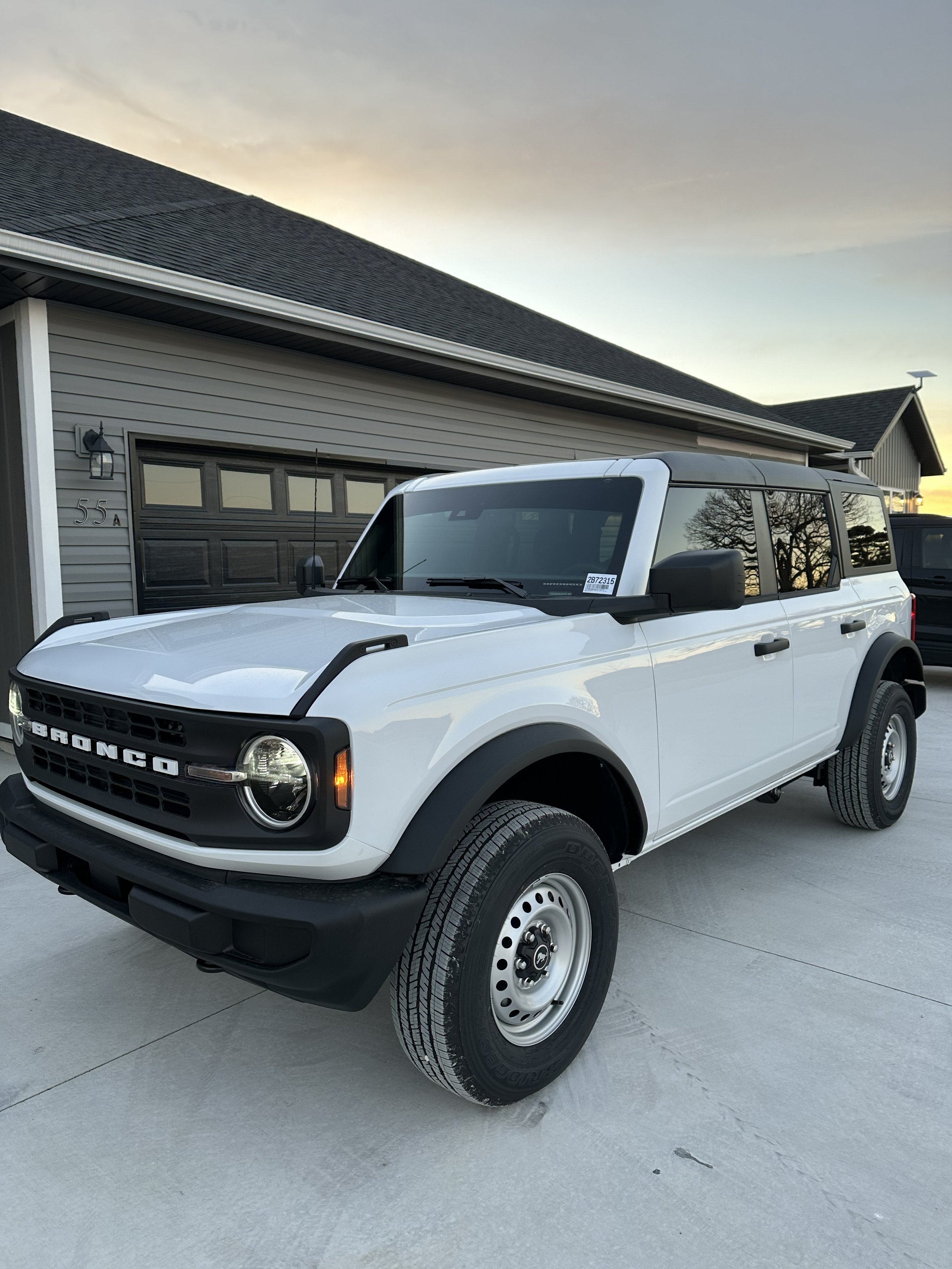 White Ford Bronco SUV parked in front of a house with a garage at dusk.
