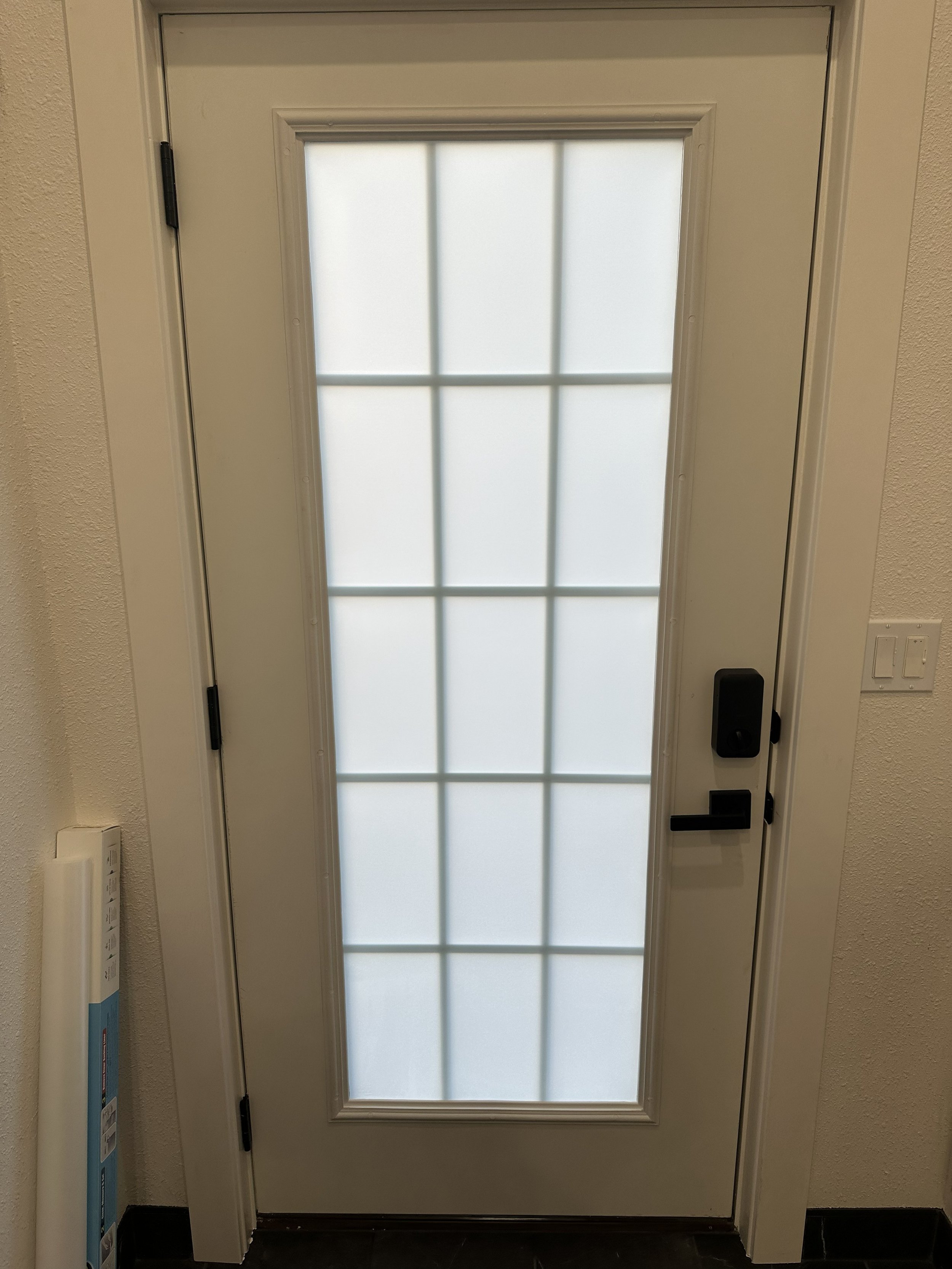 A white door with a large frosted glass panel divided into nine sections and a black handle and lock.