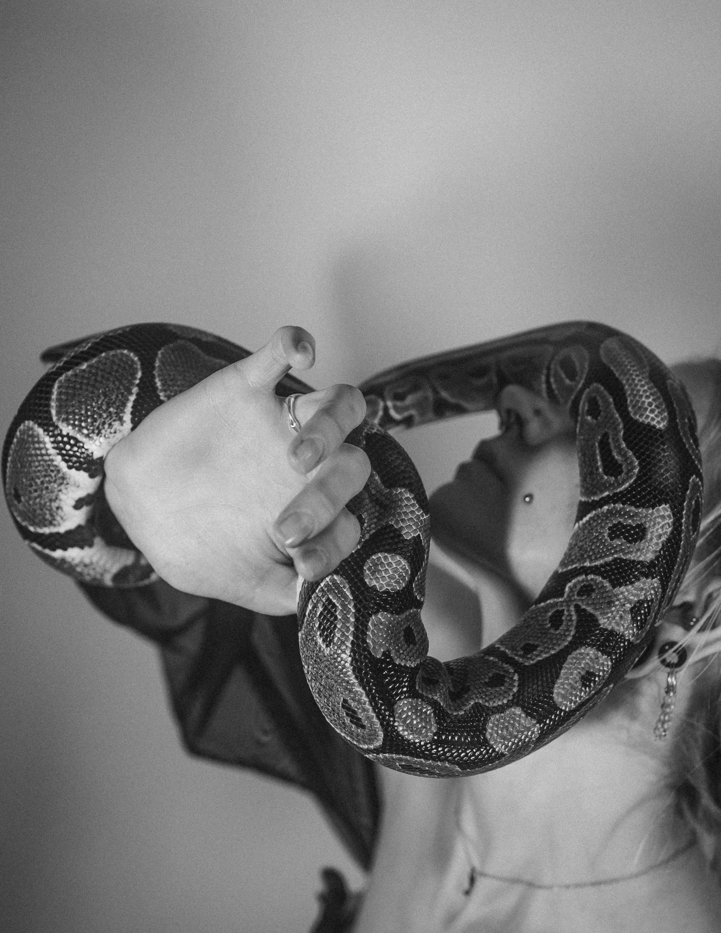 A person with a snake around their neck, holding the snake's head with their hand, black and white photograph.