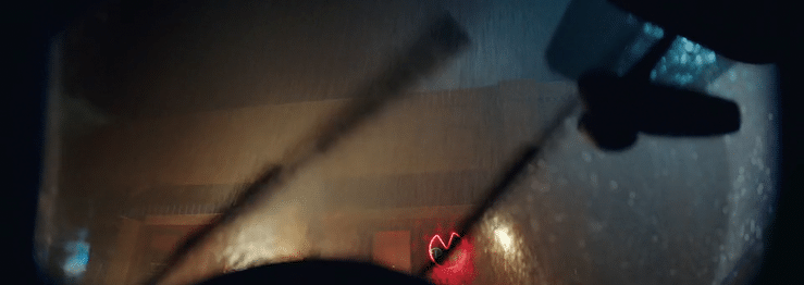 View from inside a vehicle during heavy rain at night with water streaks on the windshield and the road illuminated by streetlights.