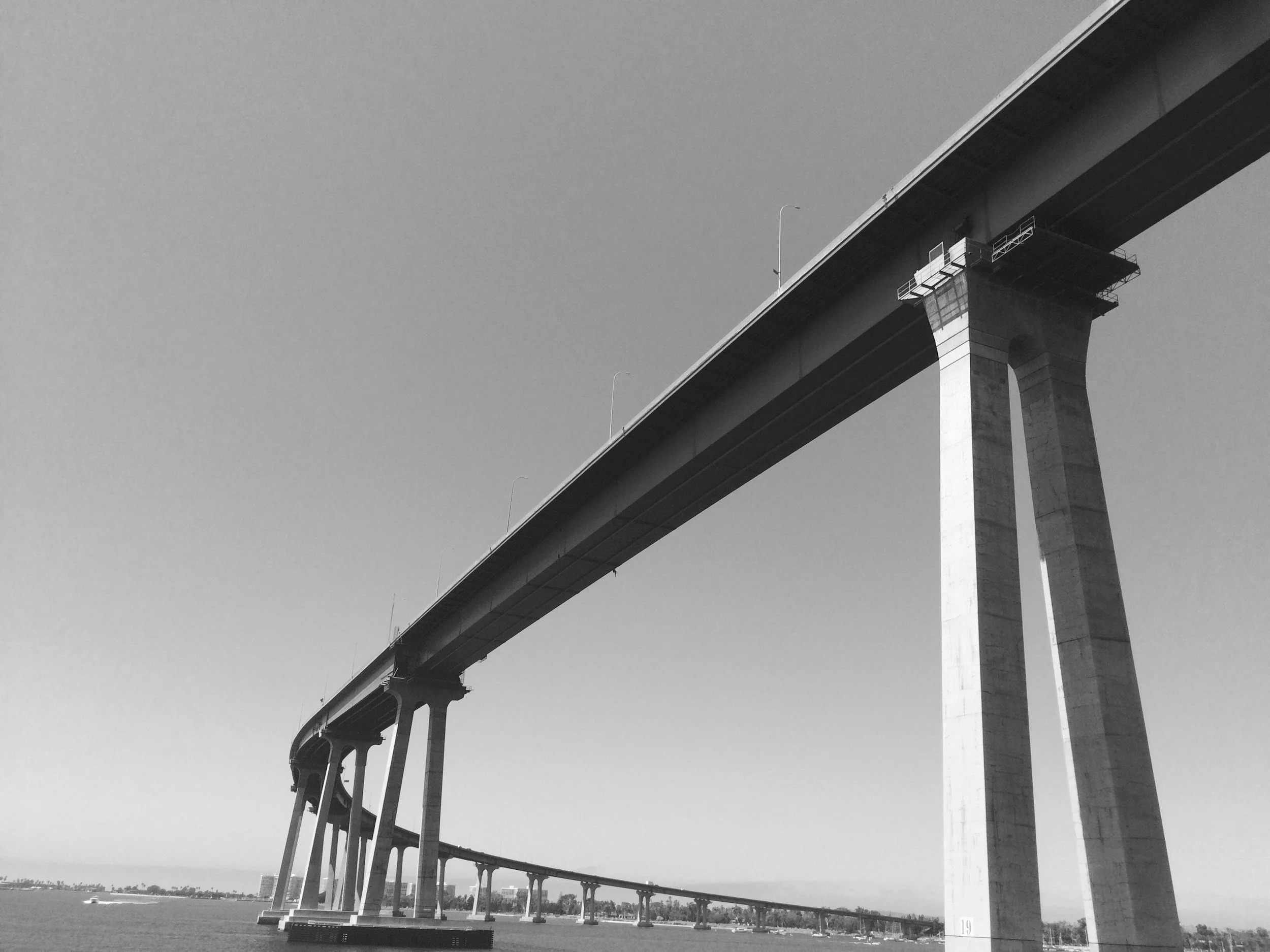 Black and white photo of a large bridge spanning over a body of water, with tall supporting pillars and an empty sky.