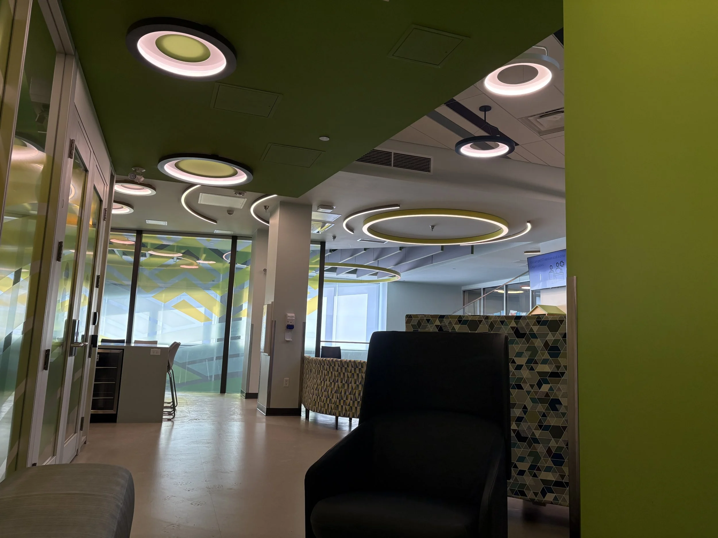 A green waiting room with chair and benches, a bright window across the way.