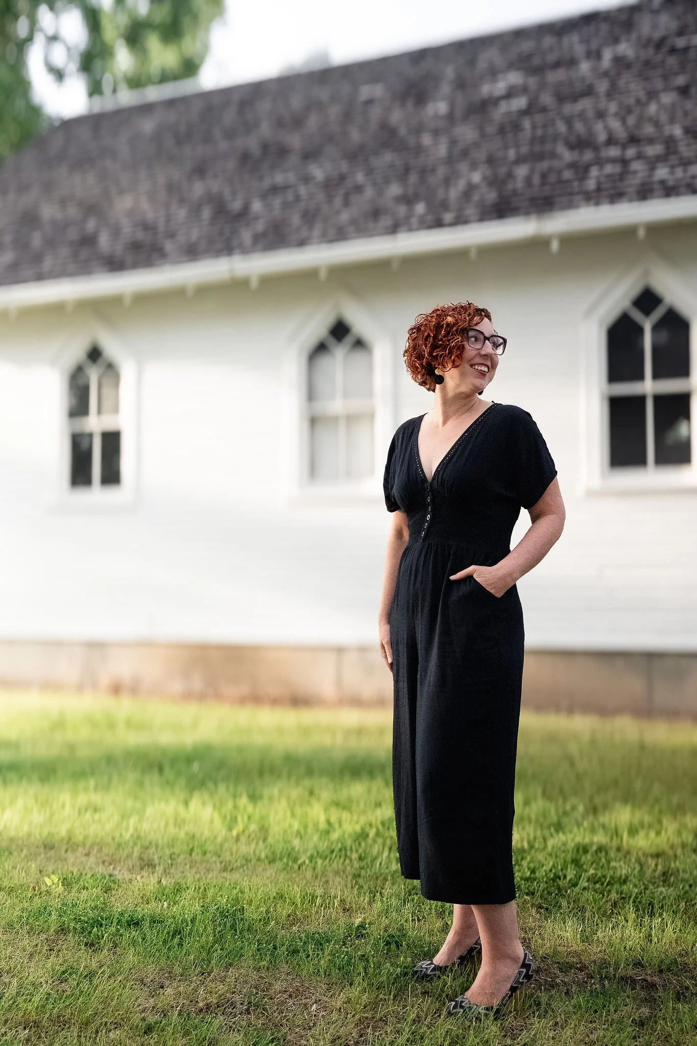 A woman with curly red hair, green glasses, and a checkered jacket sitting in front of Christmas decorations including a wreath with pink candles and nativity figurines.