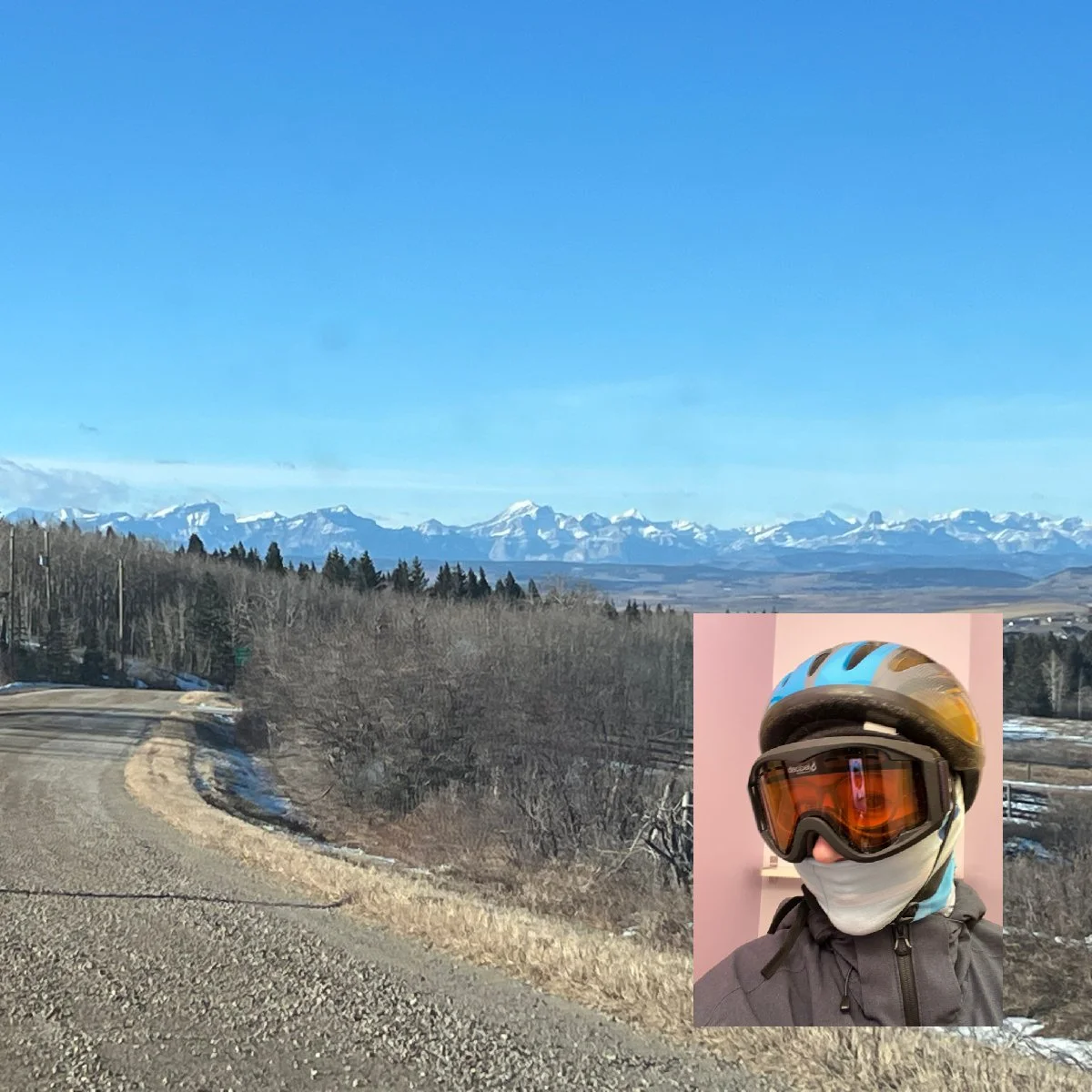 Road heading to Mount St. Francis Retreat Centre, with the Mountains on the horizon, and a blue sky overhead. Inset, a photo of Leah with her bike helmet, ski goggles and scarf over her face.