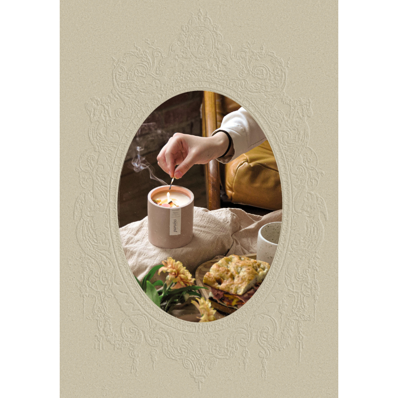 A photo person lighting a candle in a cozy setting with a sandwich, flowers, and a cup inside an embossed, ornate frame.