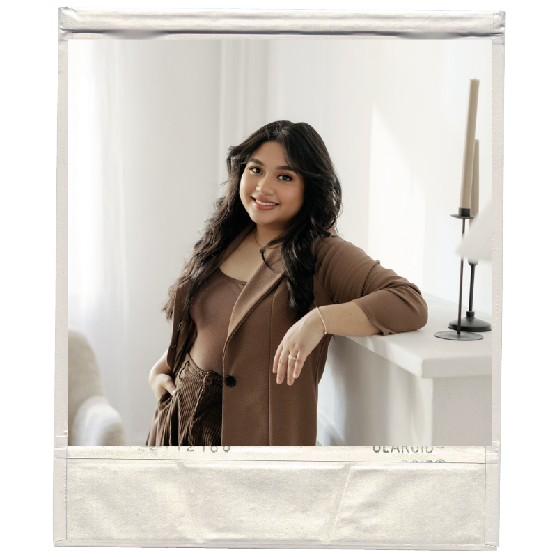 A young woman with long dark hair smiling, leaning against a white mantle, in a well-lit room with white curtains and modern decor.