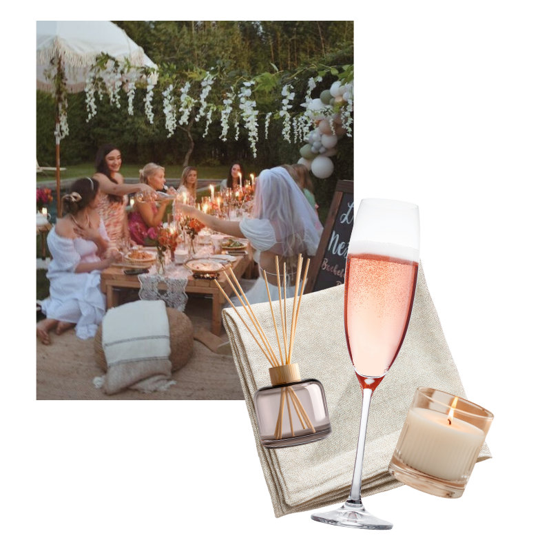 A group of people having a dinner party outdoors during the evening. There are candles on the table, and decorations including white flowers and balloons overhead. Outside of the photo , there is a linen napkin, diffuser, champagne glass and candle.