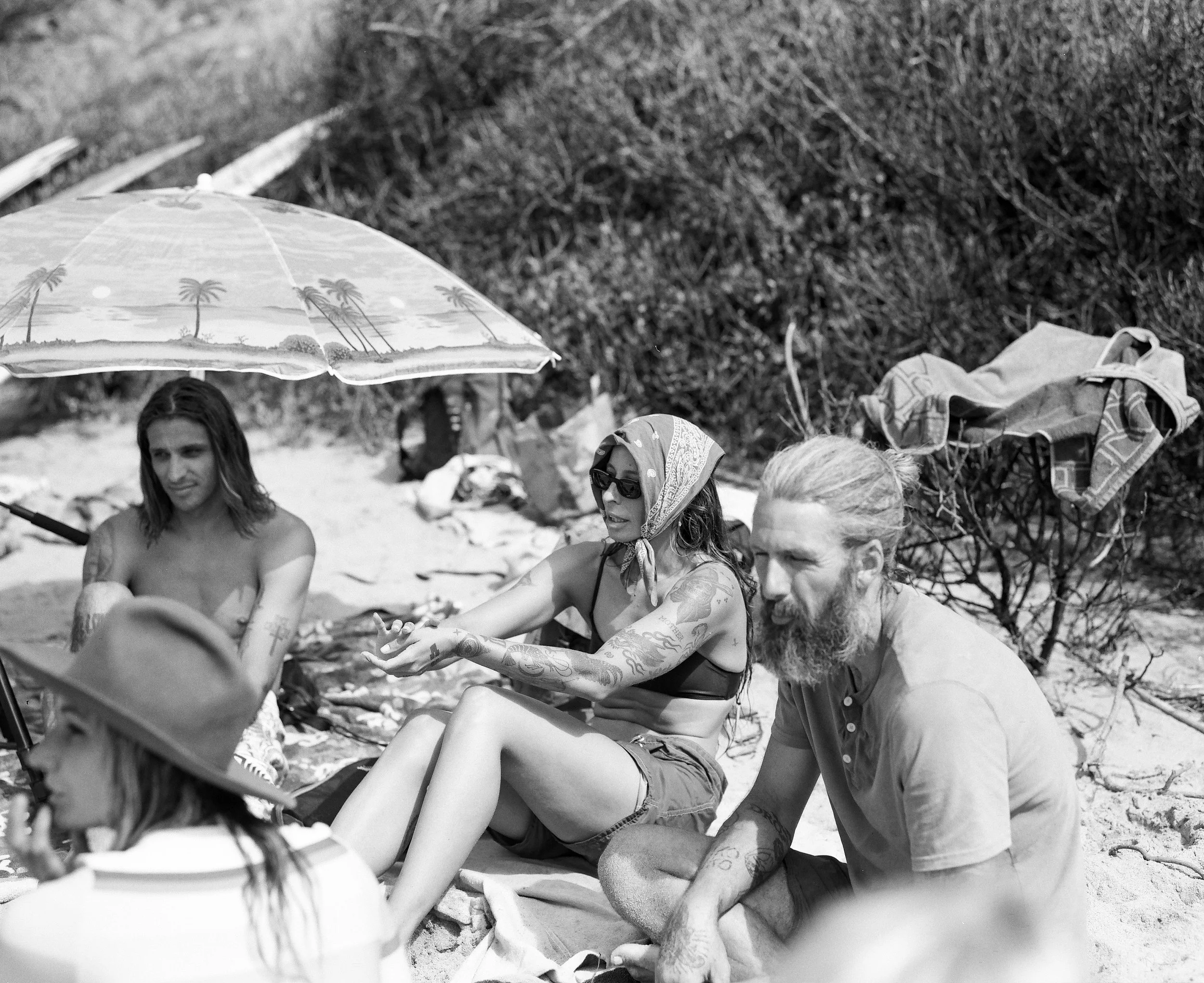 Group of people sitting on the beach under an umbrella, relaxing.