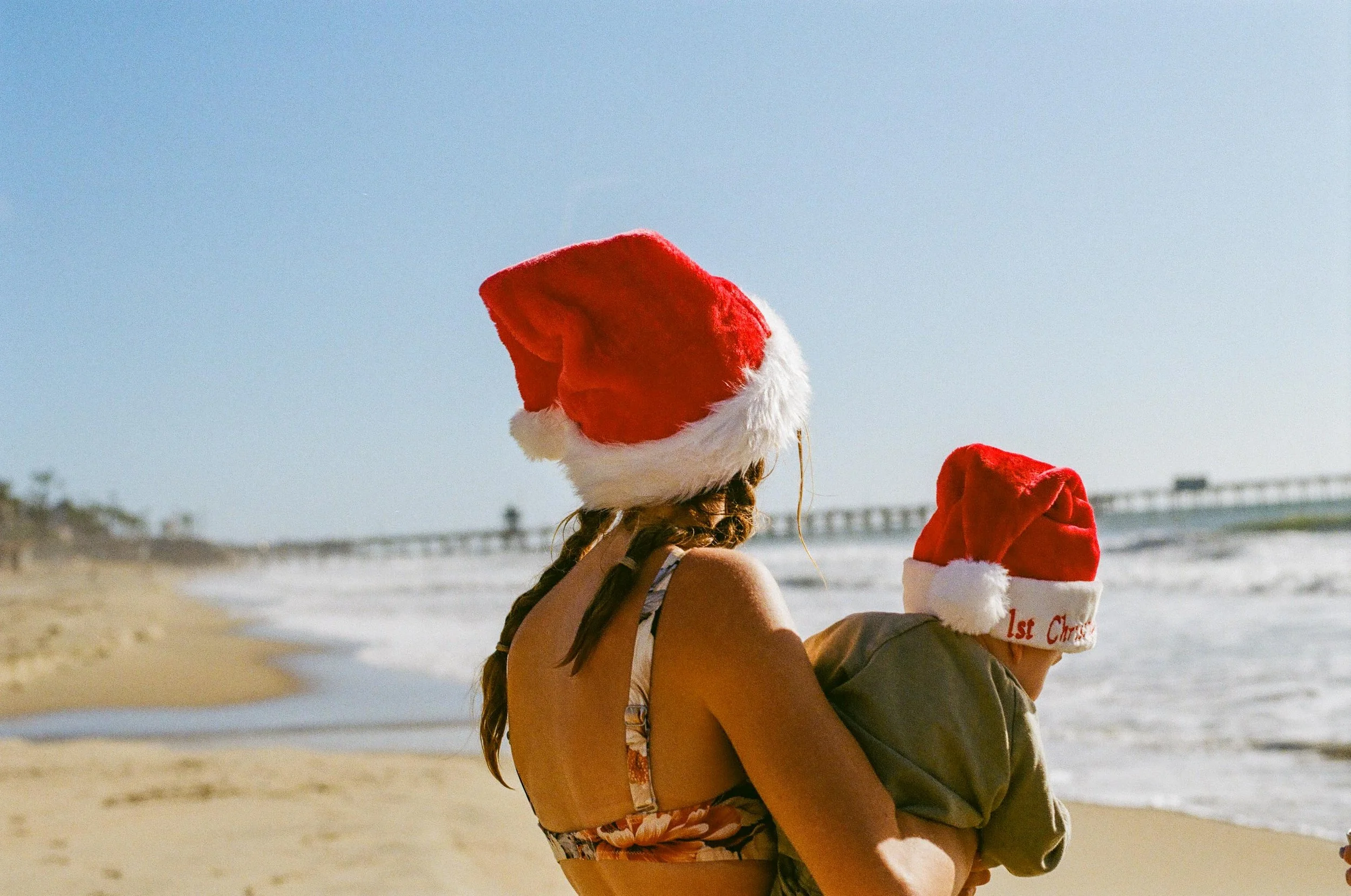 A woman and a child wearing Santa hats at the beach.