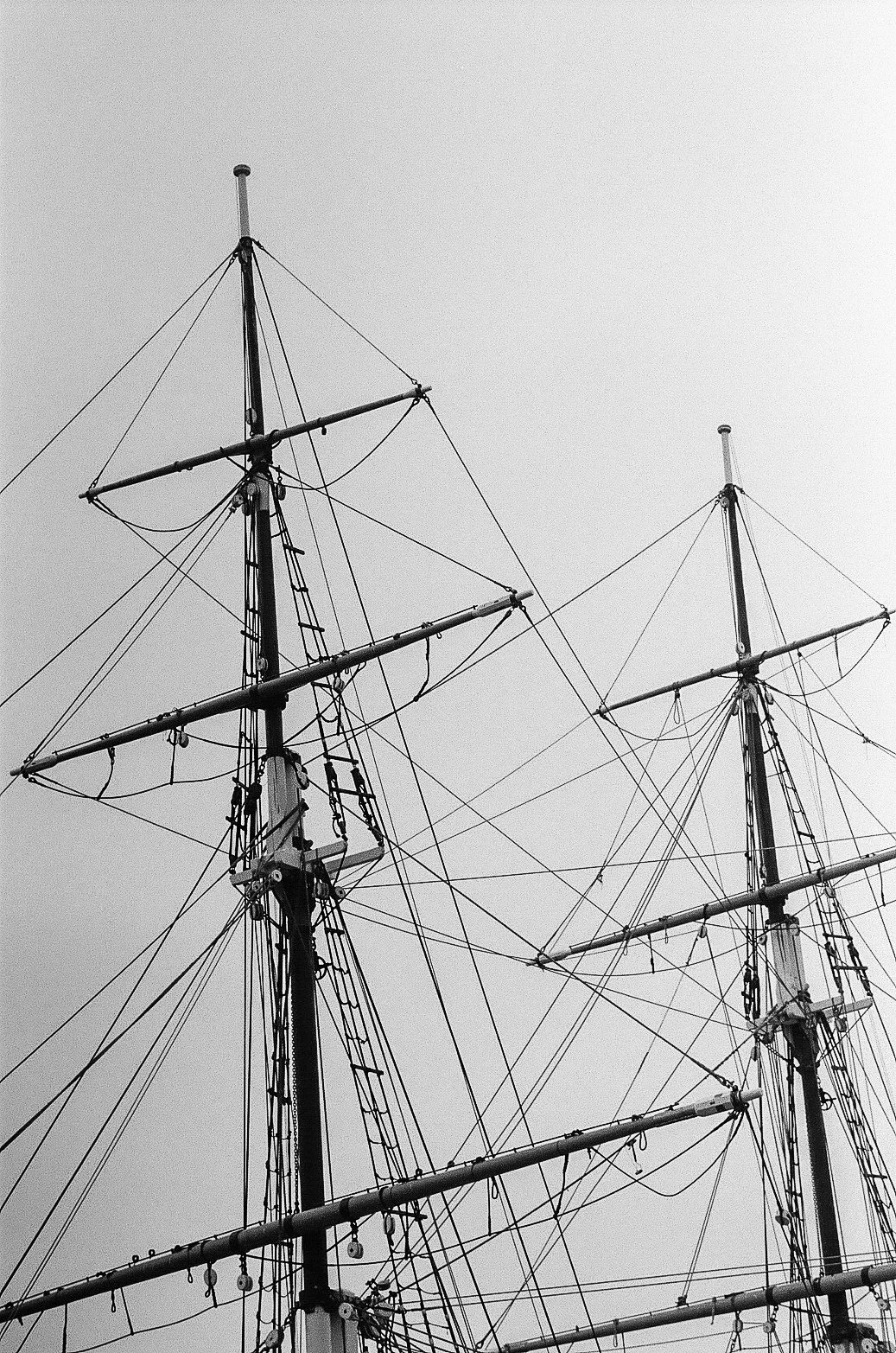 Black and white photo of the masts and rigging of a tall ship against the sky.
