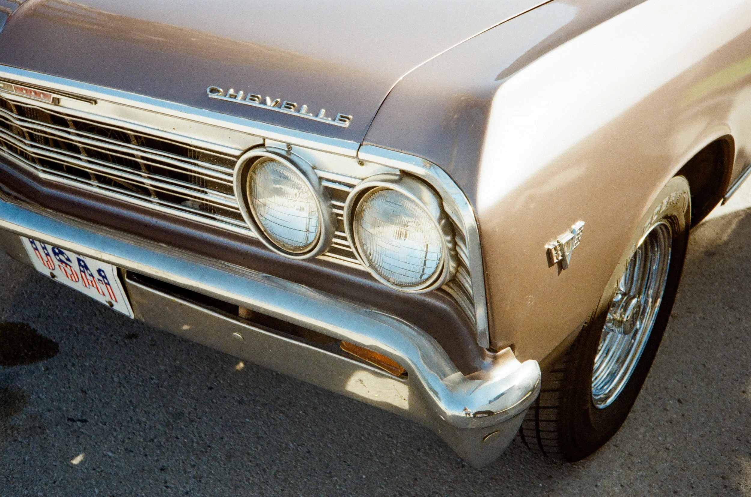 Close-up of a vintage Chevrolet car's front end with round headlights and chrome details, parked on asphalt.