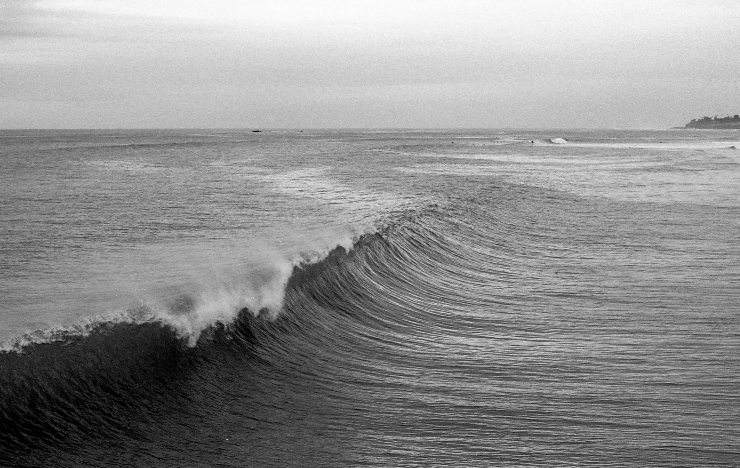 Black and white photo of ocean waves with a shoreline in the distance.