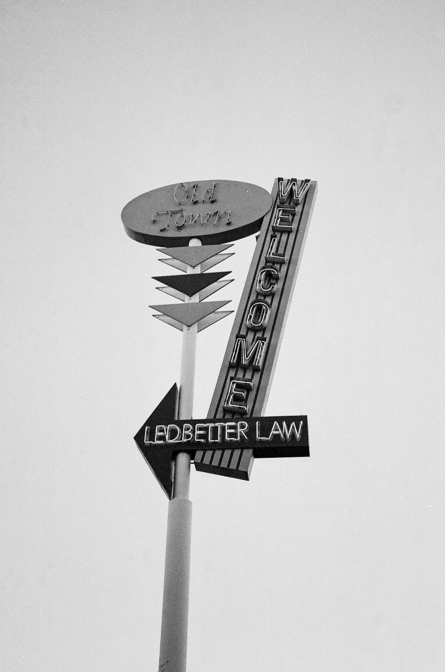Vintage neon motel sign with the words 'Old Town,' 'Motel,' and 'LED Better Law' pointing left, set against a clear sky.