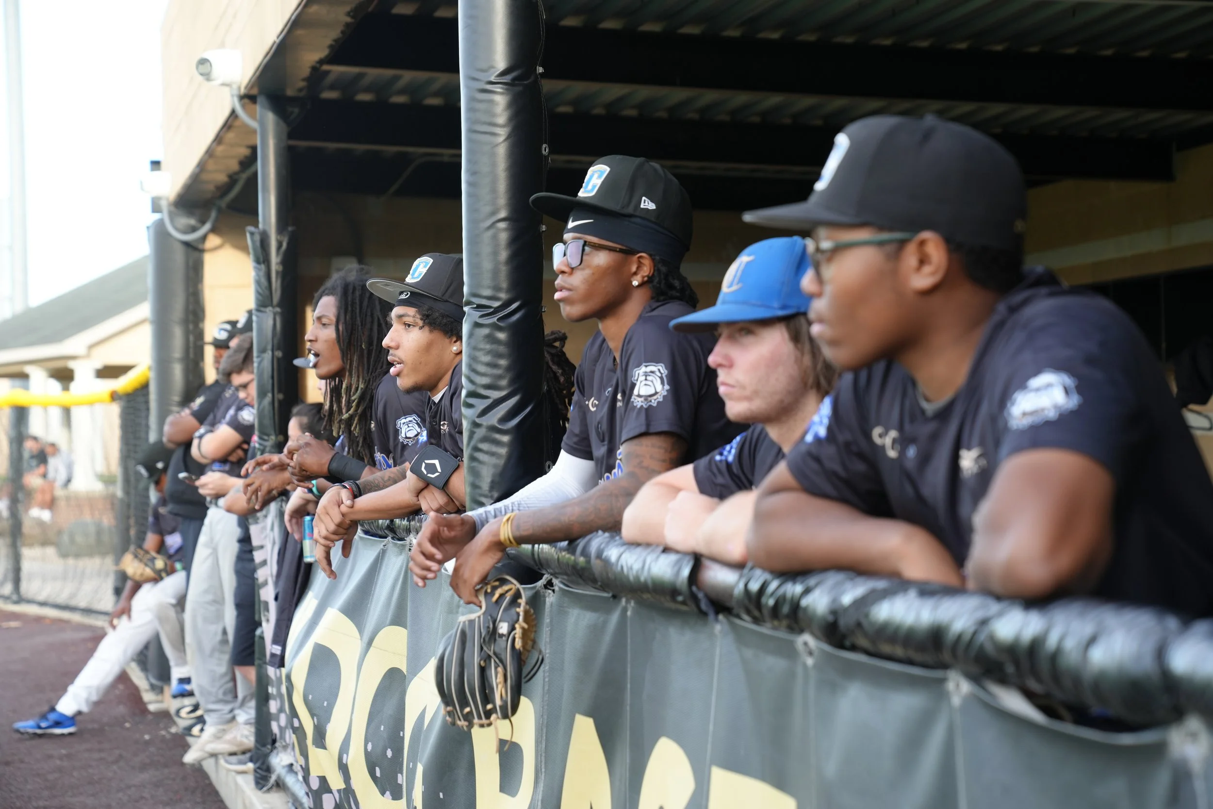 Baseball players in team uniforms and caps inside the dugout during a game.