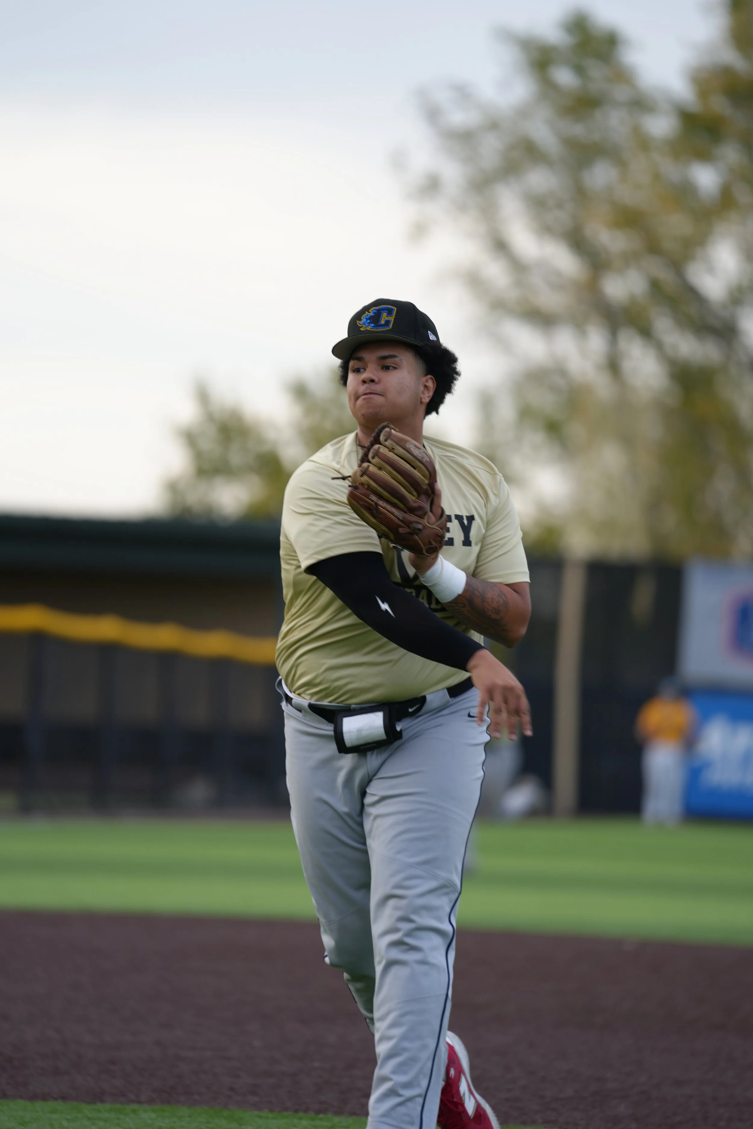A young male baseball player running on the field, wearing a baseball cap, uniform, and glove, with a focused expression.