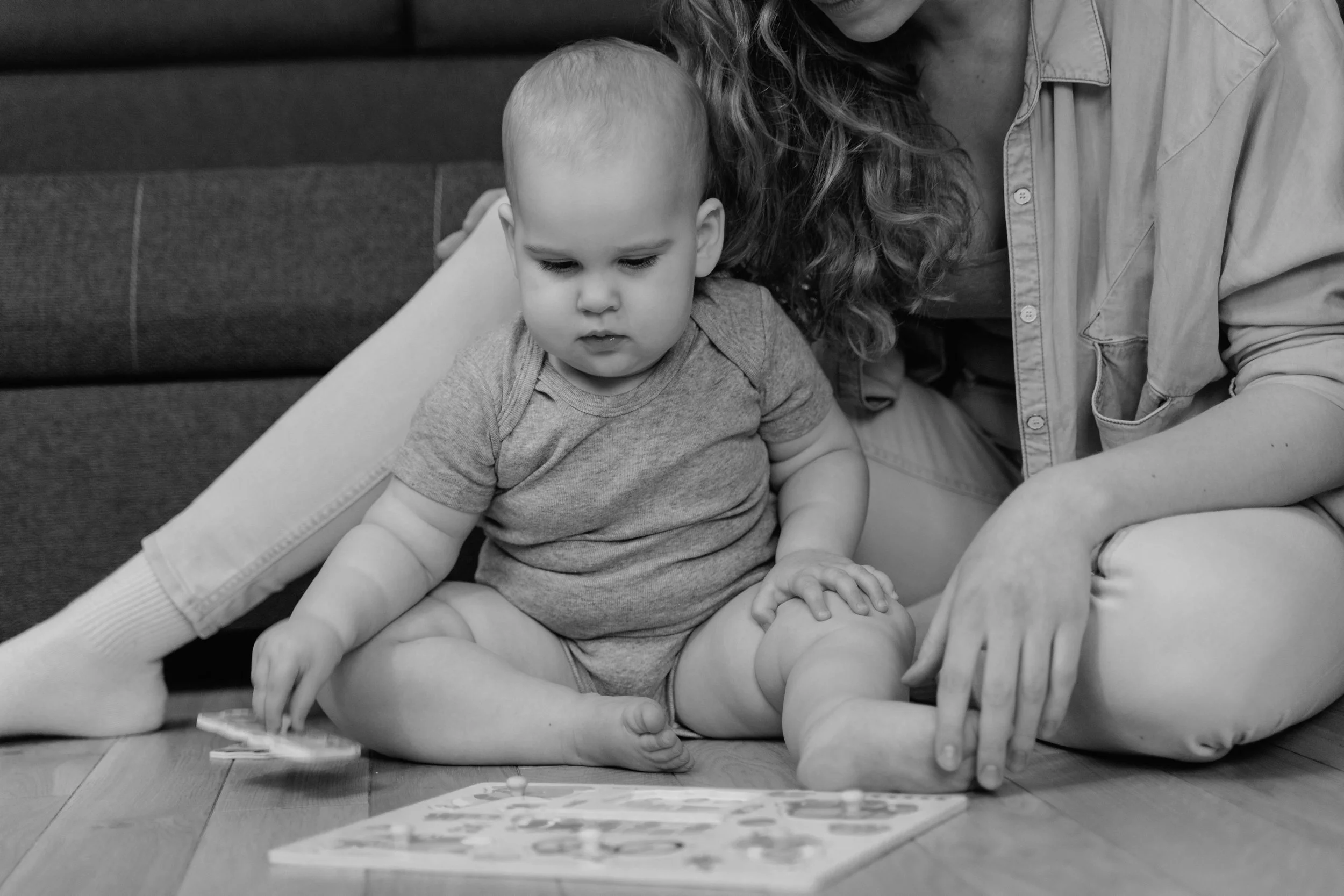 A close-up black-and-white photo of a smiling adult woman and a young child, with the woman's face partially visible on the left and the child's face centered, showing large eyes and parted lips.