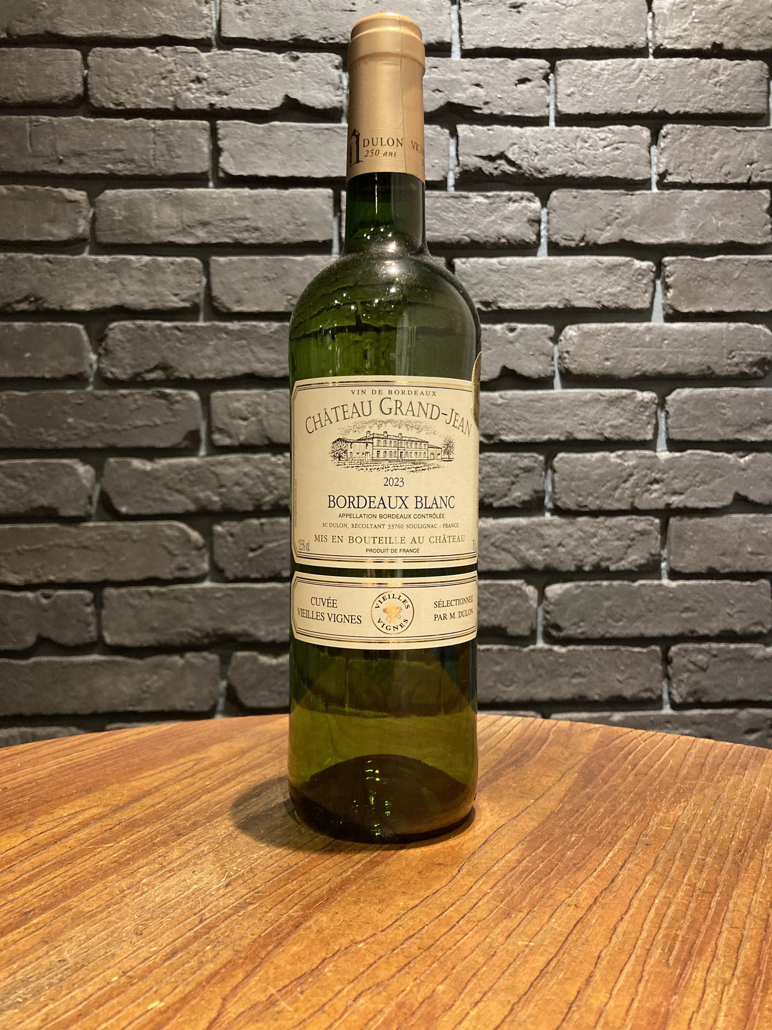 緑色のワインボトルが木製のテーブルの上に立っている。背景は灰色のレンガ壁。