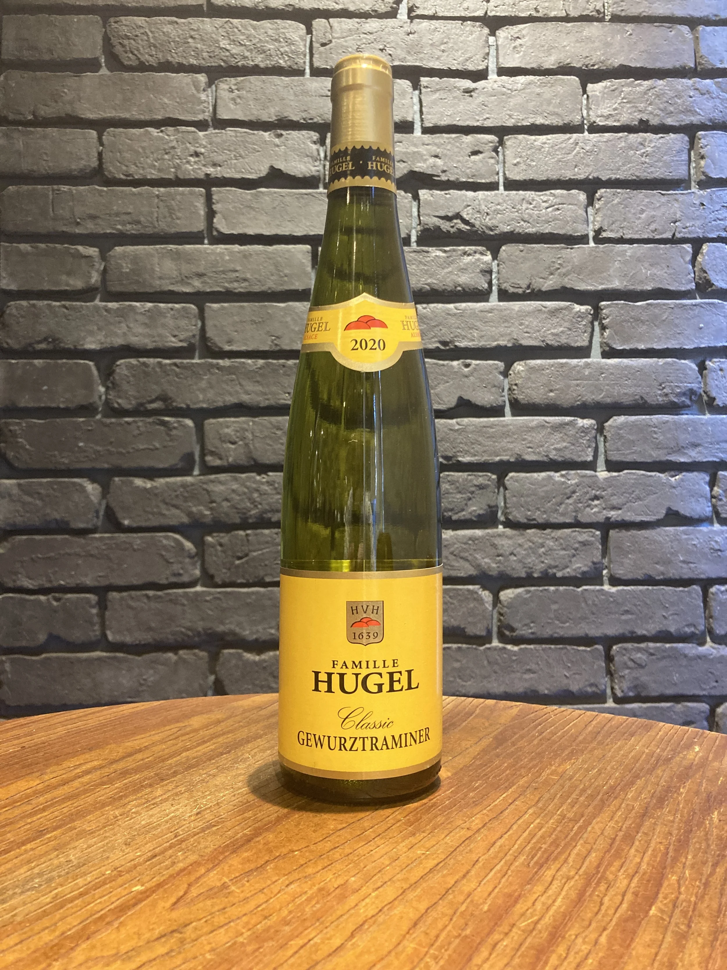 黄色いラベルのワイン瓶が木製のテーブルの上に置かれている。背景は灰色のレンガの壁。