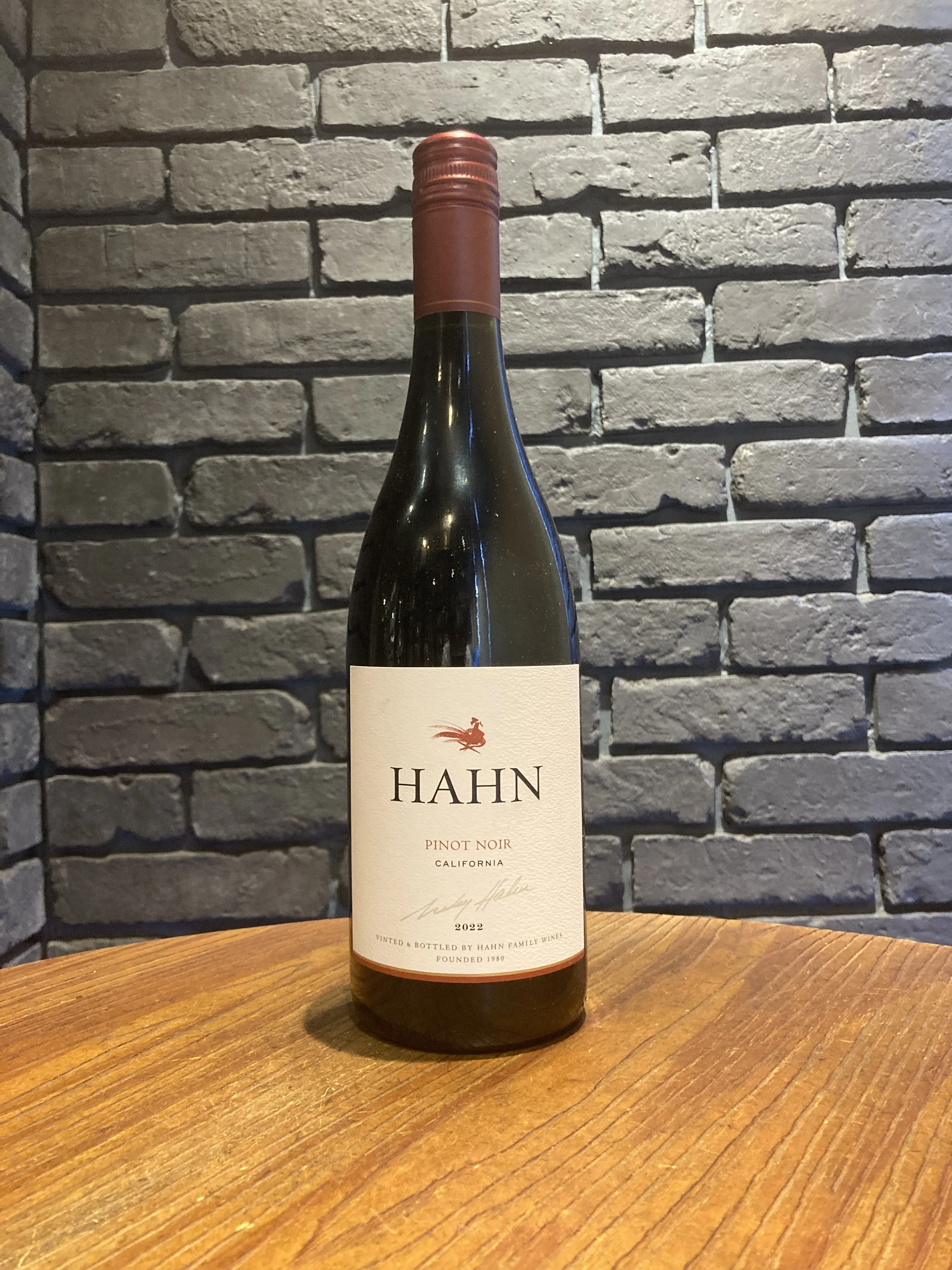 ハーンのピノノワールワインの瓶が木製のテーブルに置かれ、レンガの壁の背景が映っている
