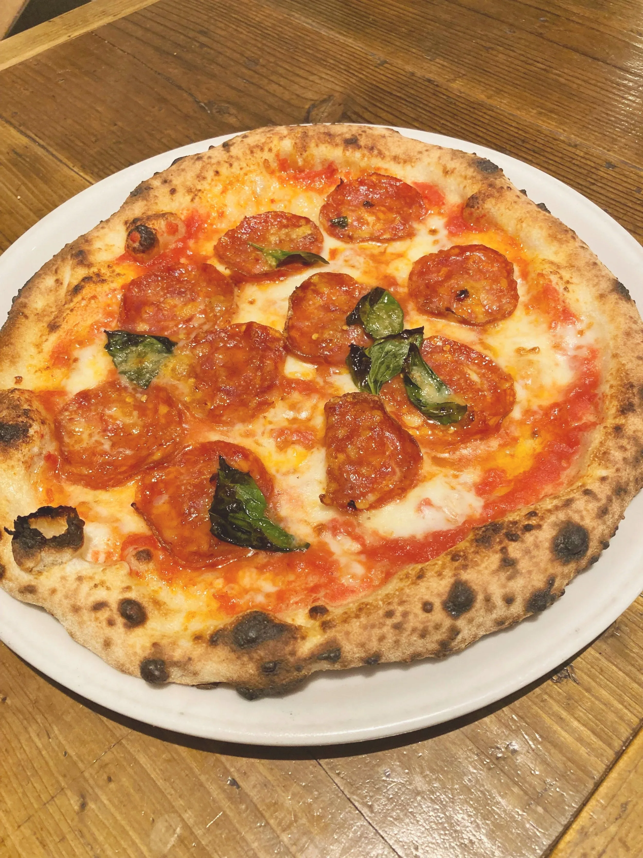 ピザ。トマトソース、チーズ、サラミ、バジルがのっている。