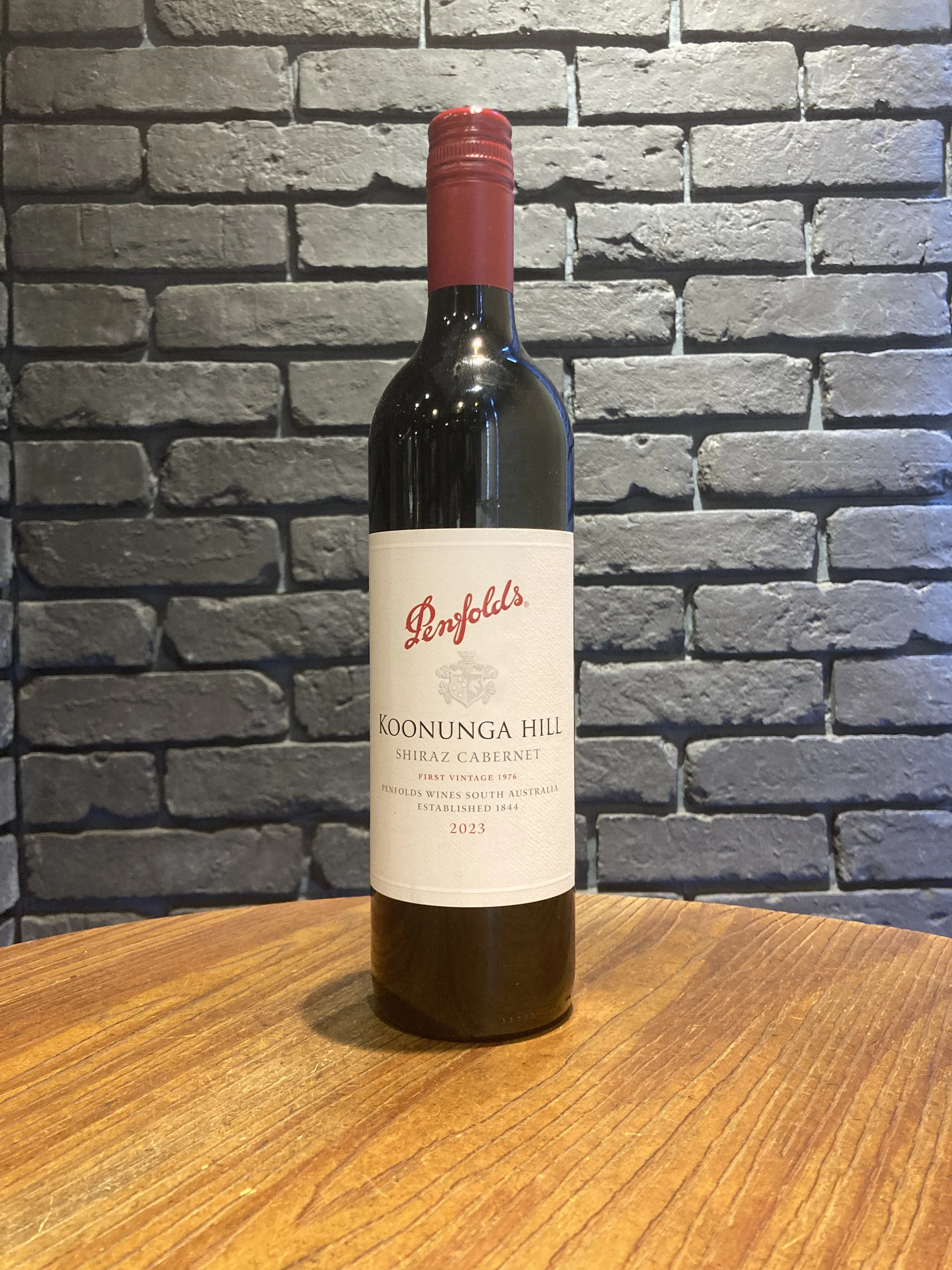 ワインのボトルが木製のテーブルに置かれている写真。背後は灰色のレンガ壁。