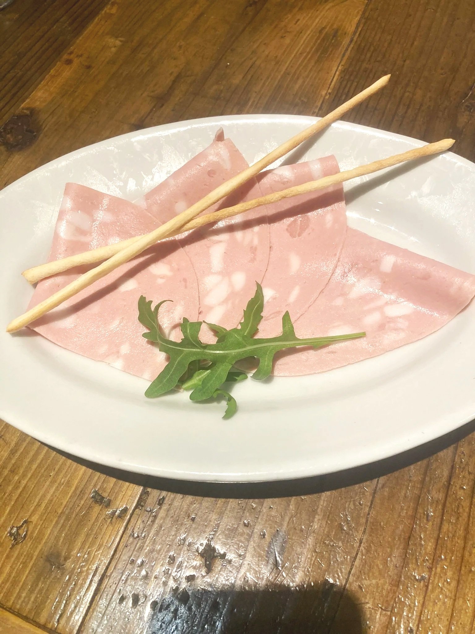 ハムとサラダ菜、クラッカーが盛り付けられた白い皿が木製のテーブルに置かれている料理の写真