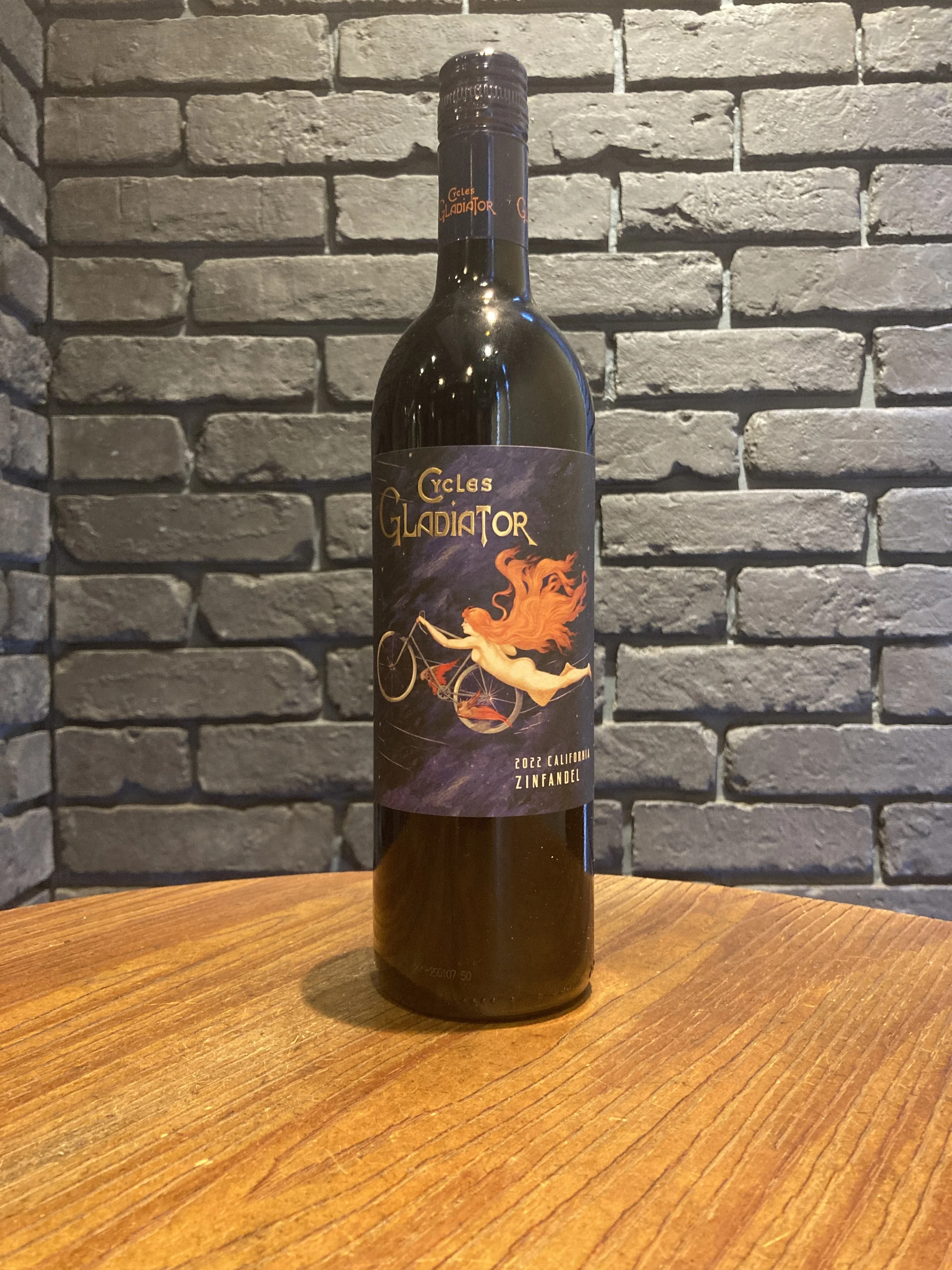 黒い瓶にラベルが貼られており、イラストで赤毛の女性が自転車に乗っている様子が描かれている。背景は暗い色調。