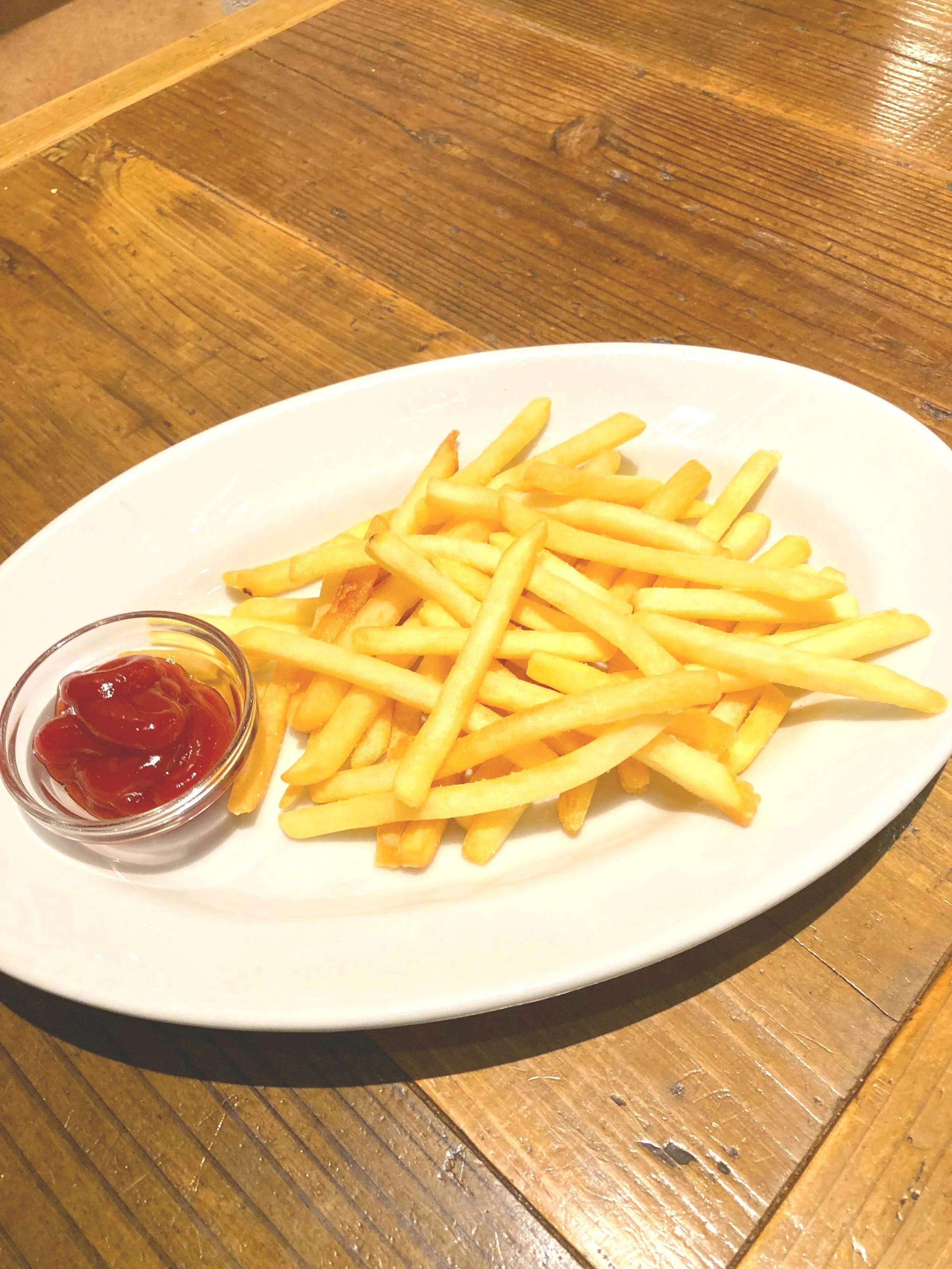 フライドポテトとケチャップが載った白い皿が木製のテーブルに置かれている写真