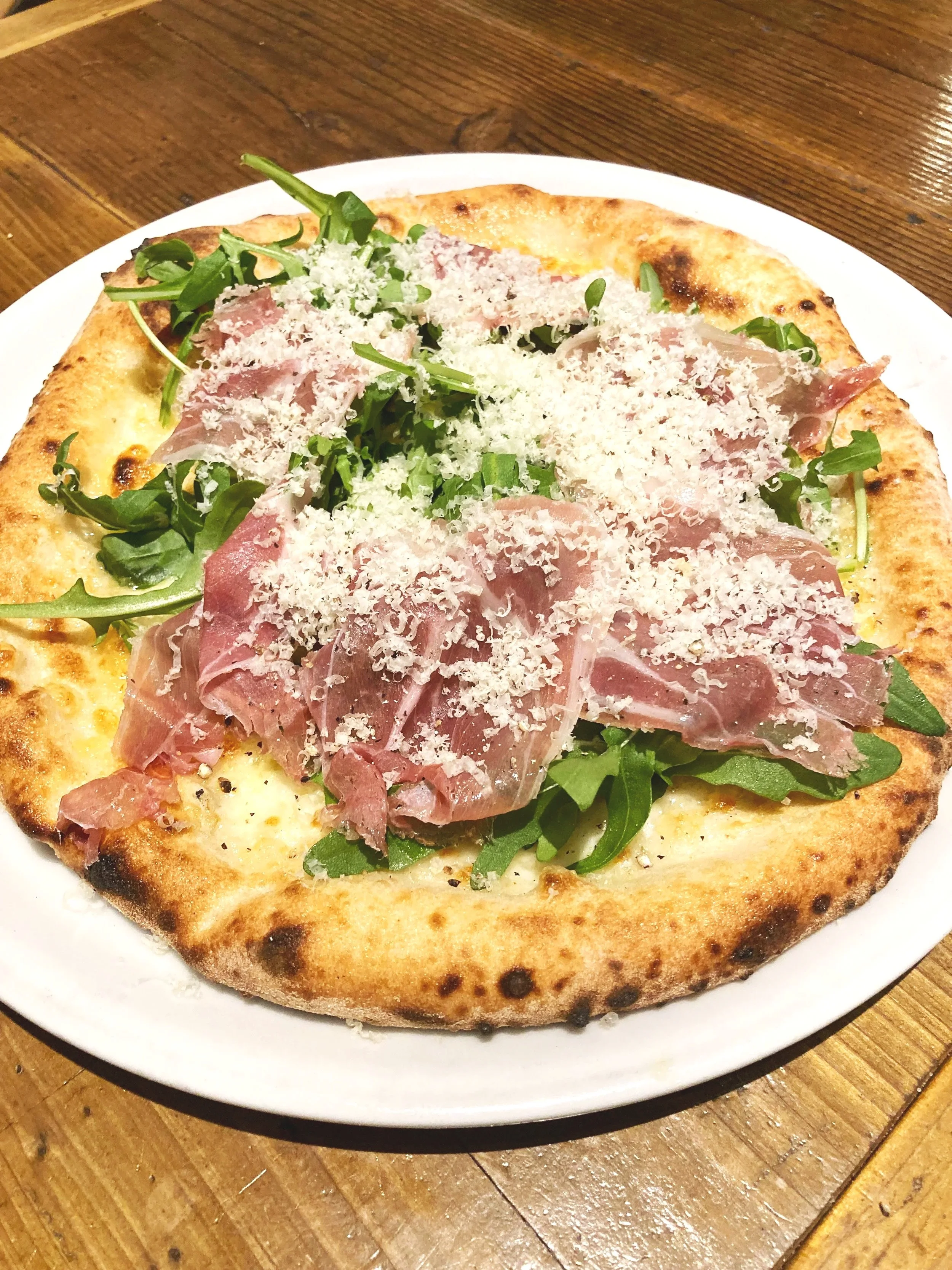 サラダピザ。ピザ生地の上にルッコラ、ハム、粉チーズがのっている。
