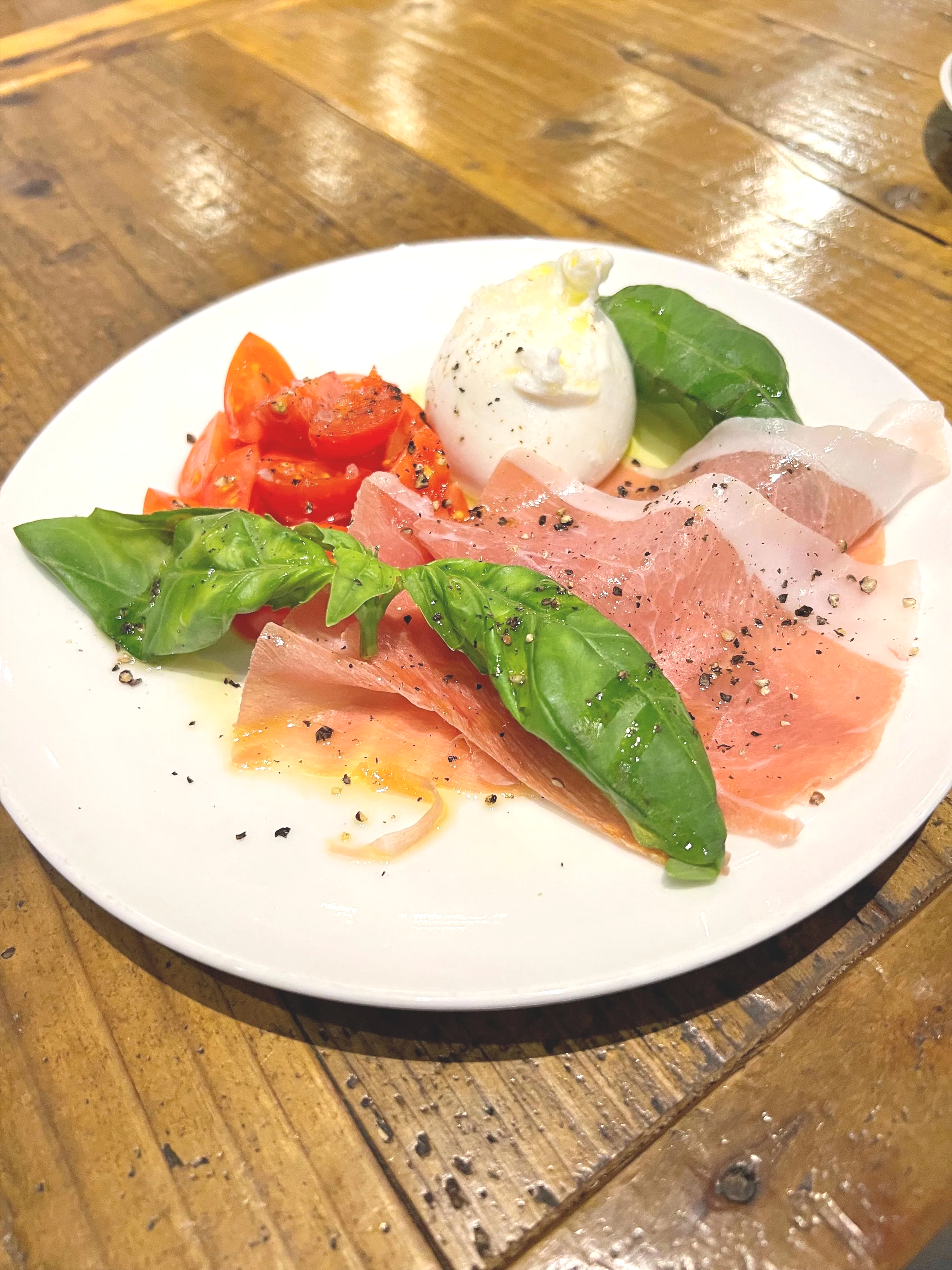 バジルの葉、トマト、モッツァレラチーズ、プロシュート、ブラックペッパー、オリーブオイルがのったカプレーゼサラダのプレート