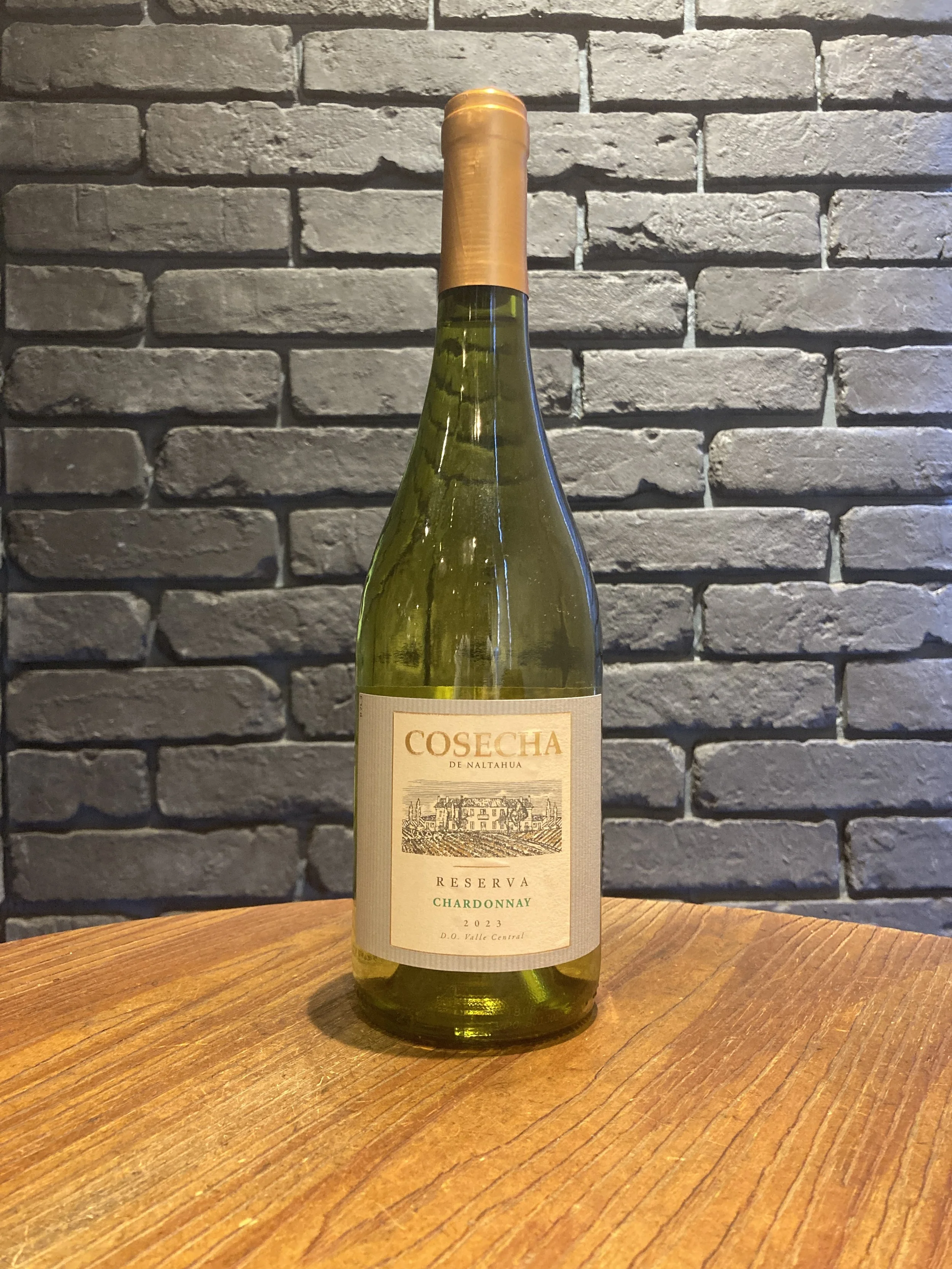 白と金色のラベルが貼られた白ワインのボトルが木製のテーブルの上に立っている。背景は灰色のレンガの壁。