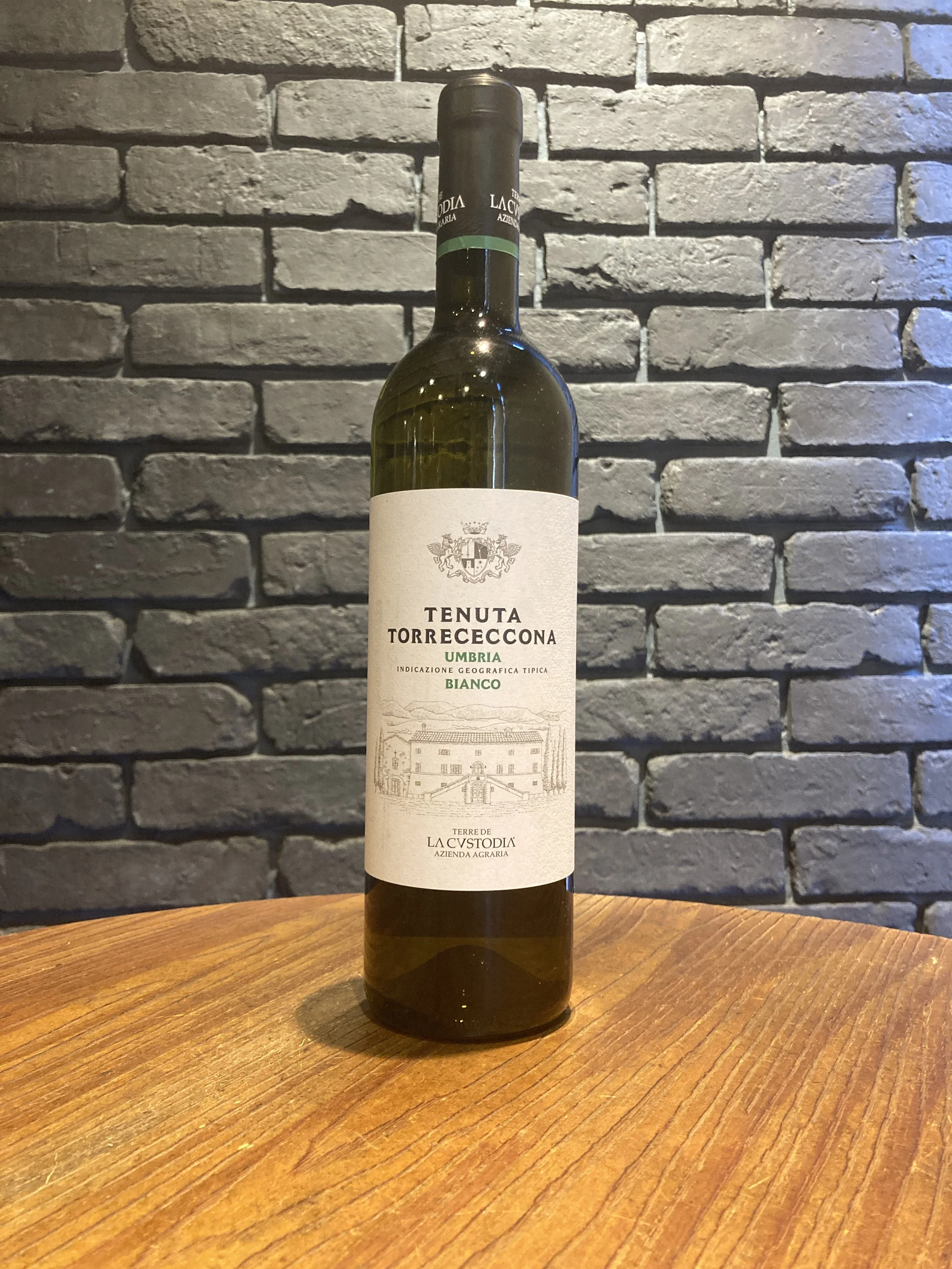 白地にイラストと文字が書かれたワインボトル。背景はレンガの壁、テーブルは木製で、ボトルは中央に置かれている。