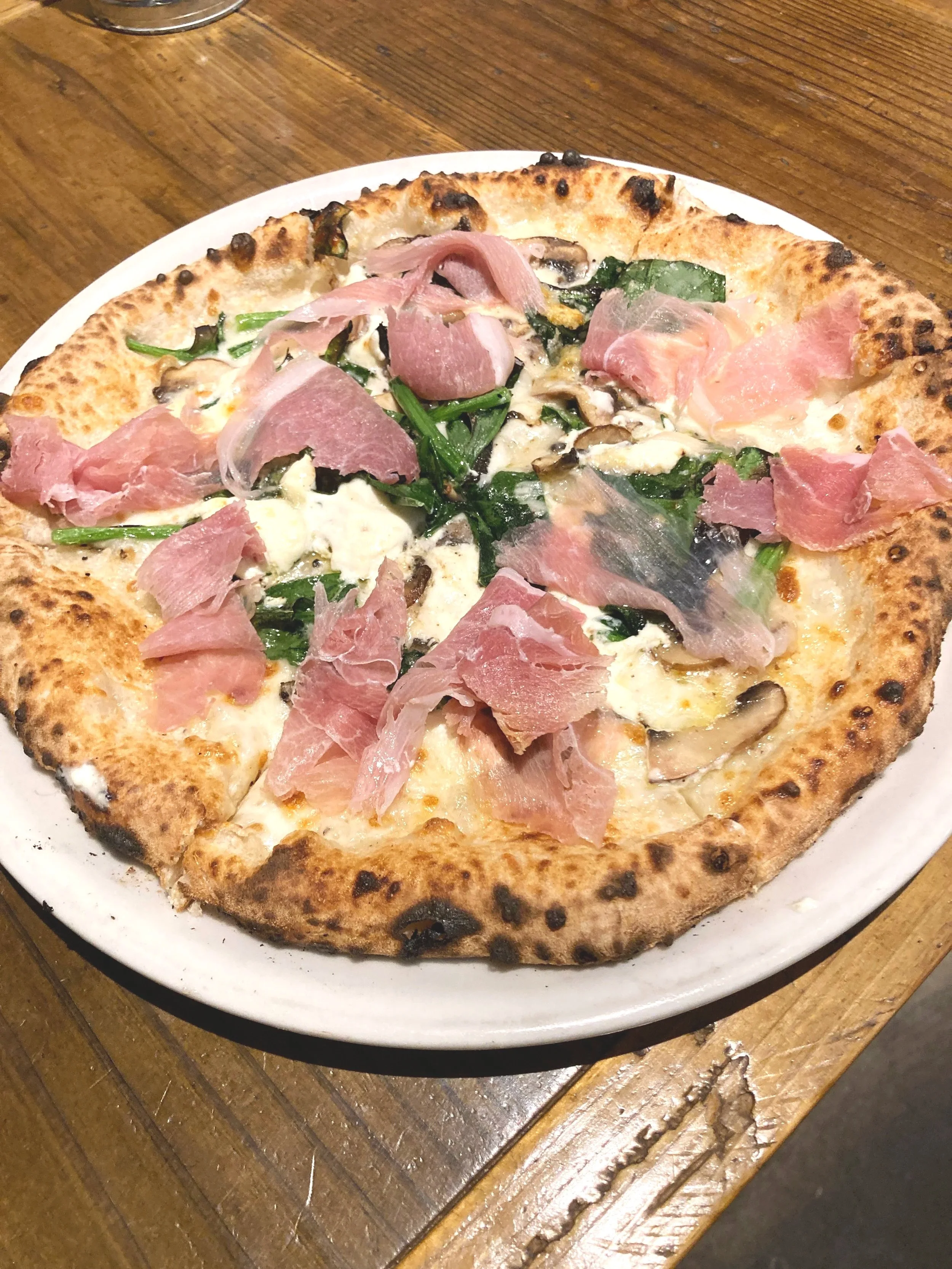 ピザの上に生ハムやきのこ、ほうれん草がのっている。