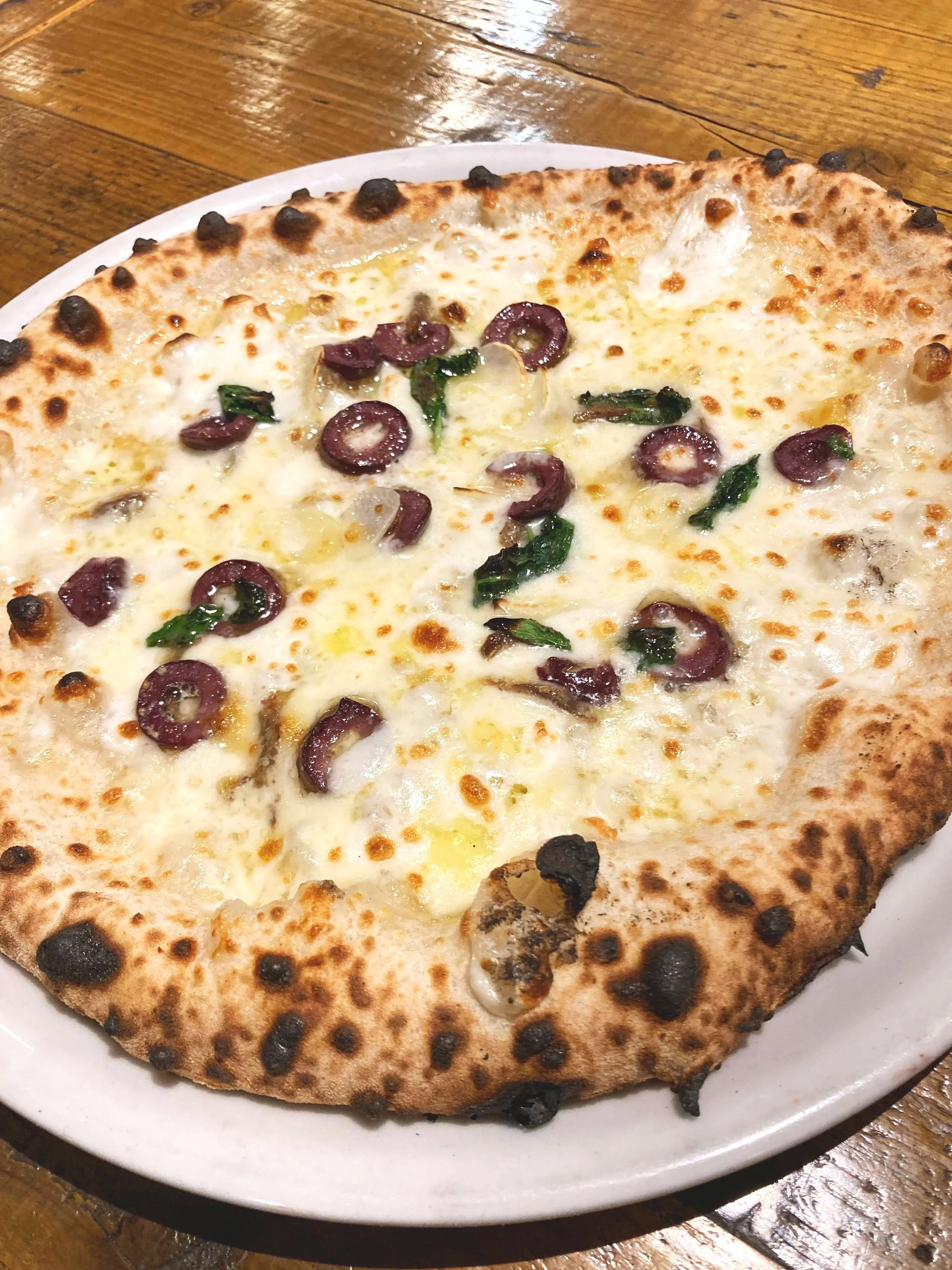 ピザの画像。チーズと黒オリーブ、バジル、ニンニクがトッピングされている。
