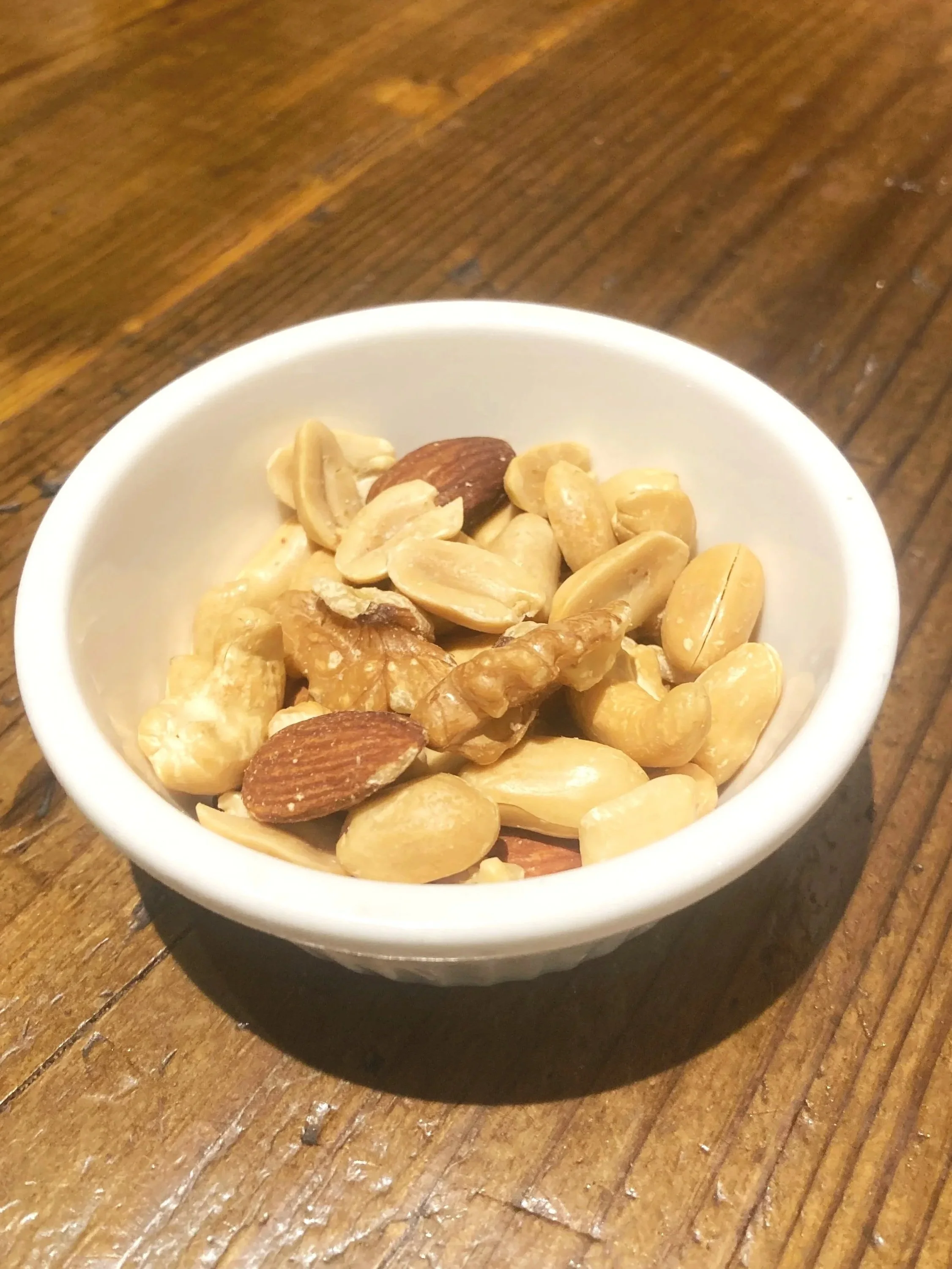 ナッツの盛り合わせが入った白い小皿、木製のテーブルの上に置かれている。