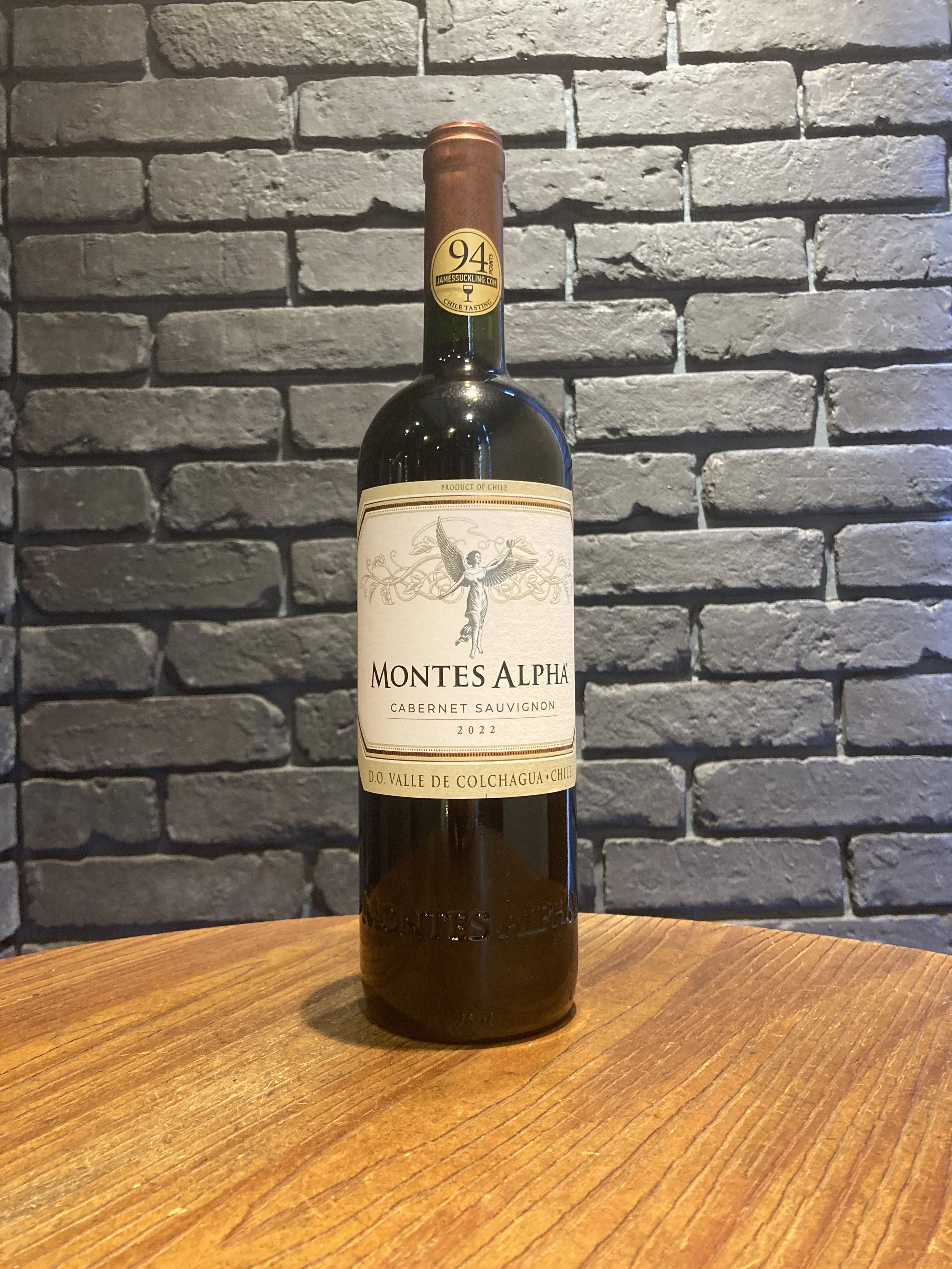 赤ワインのボトルが木製のテーブルの上に立っている。背後は灰色のレンガの壁。