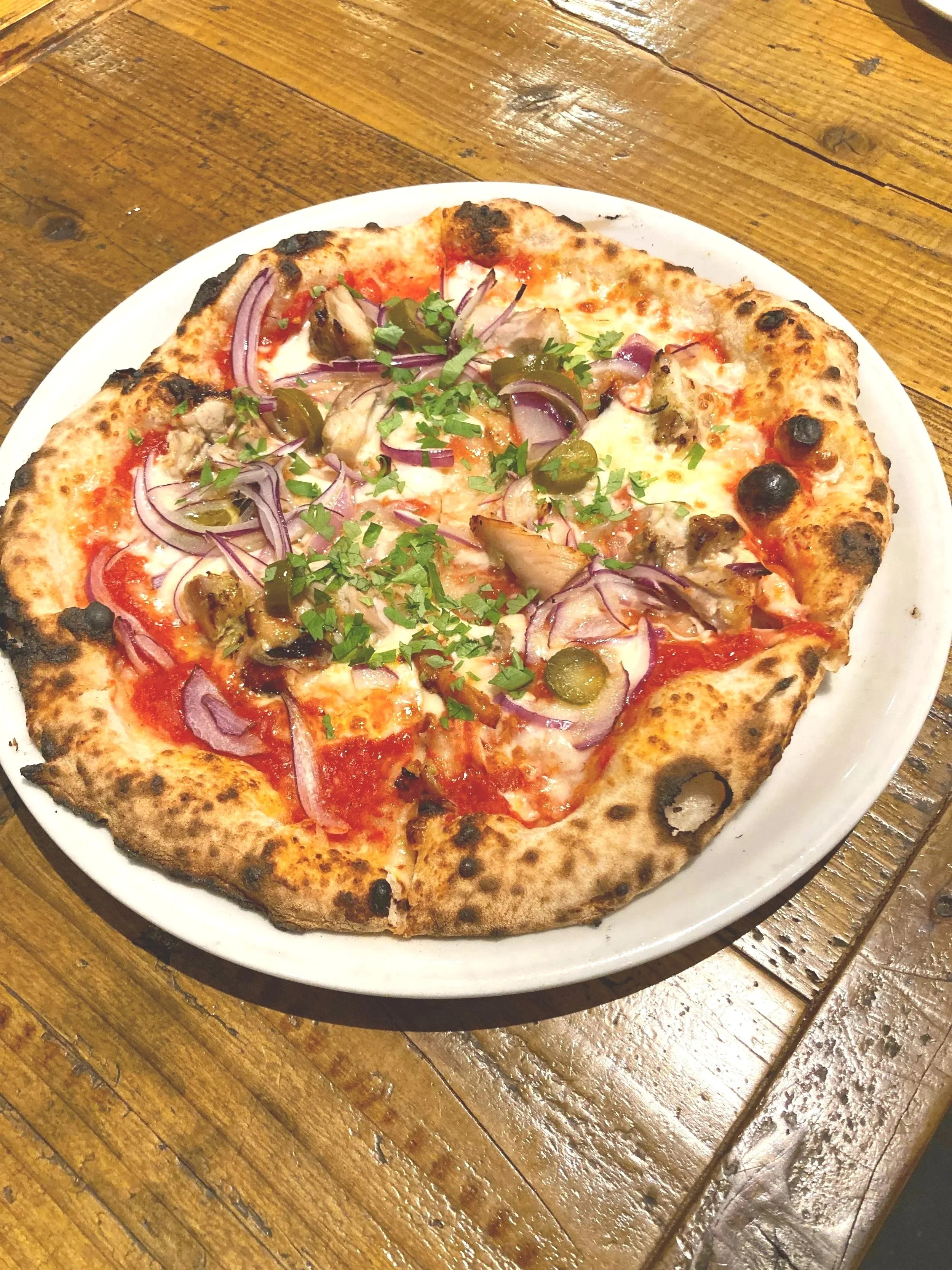 ピザが皿の上にあり、上に赤玉ねぎ、ハーブ、オリーブ、肉が乗っている。